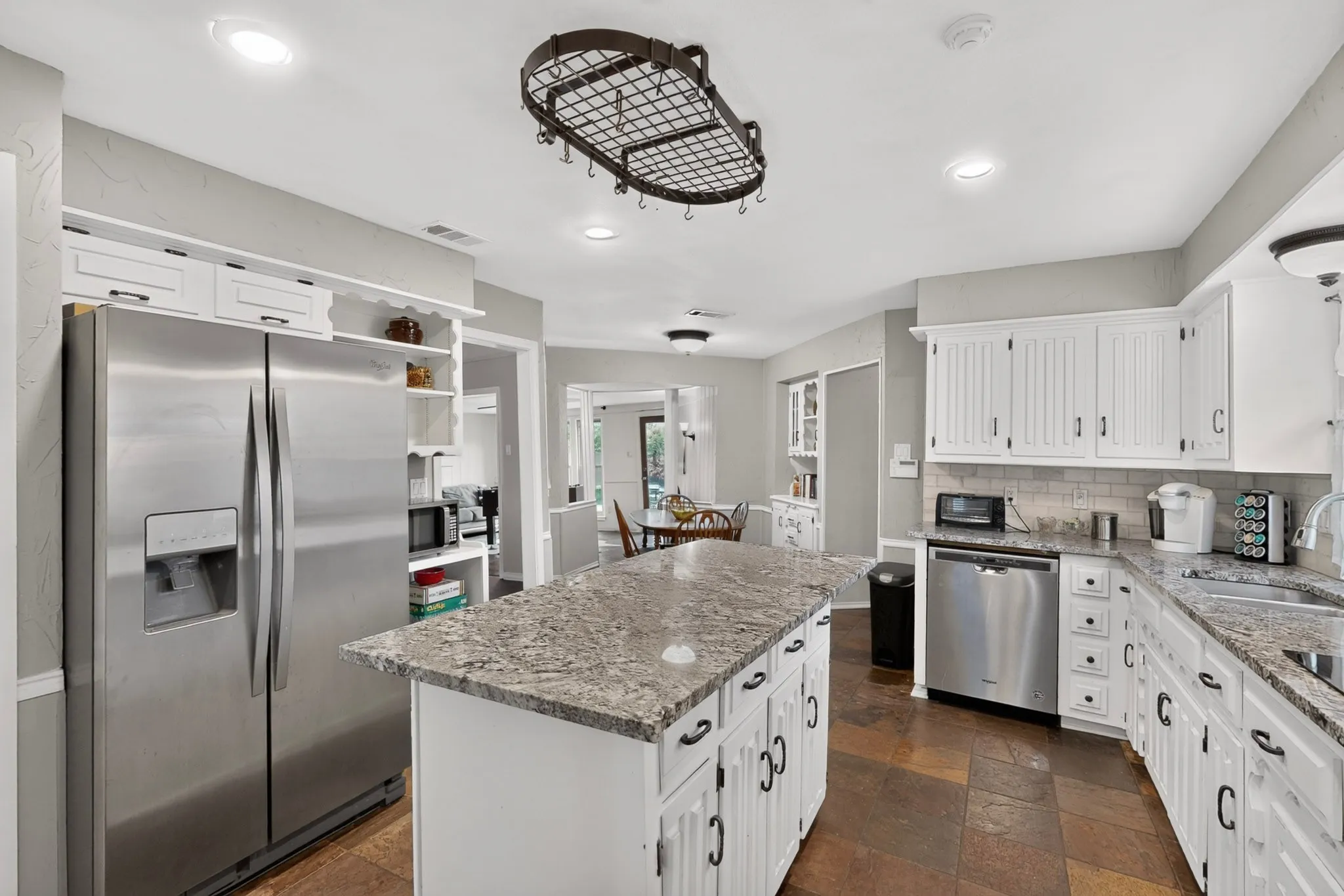 Kitchen featuring an island with stone countertop, white cabinetry with dark hardware, stainless steel appliances, tile flooring, and recessed lighting