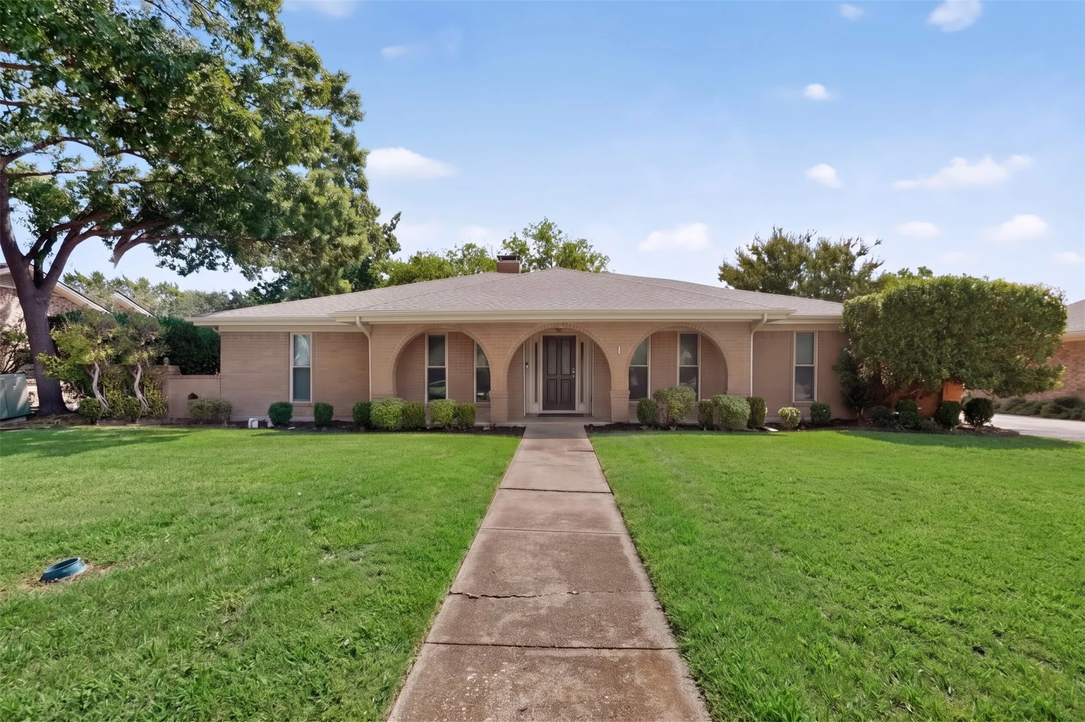 Brick exterior with arched entryway, a pitched roof, and a concrete walkway