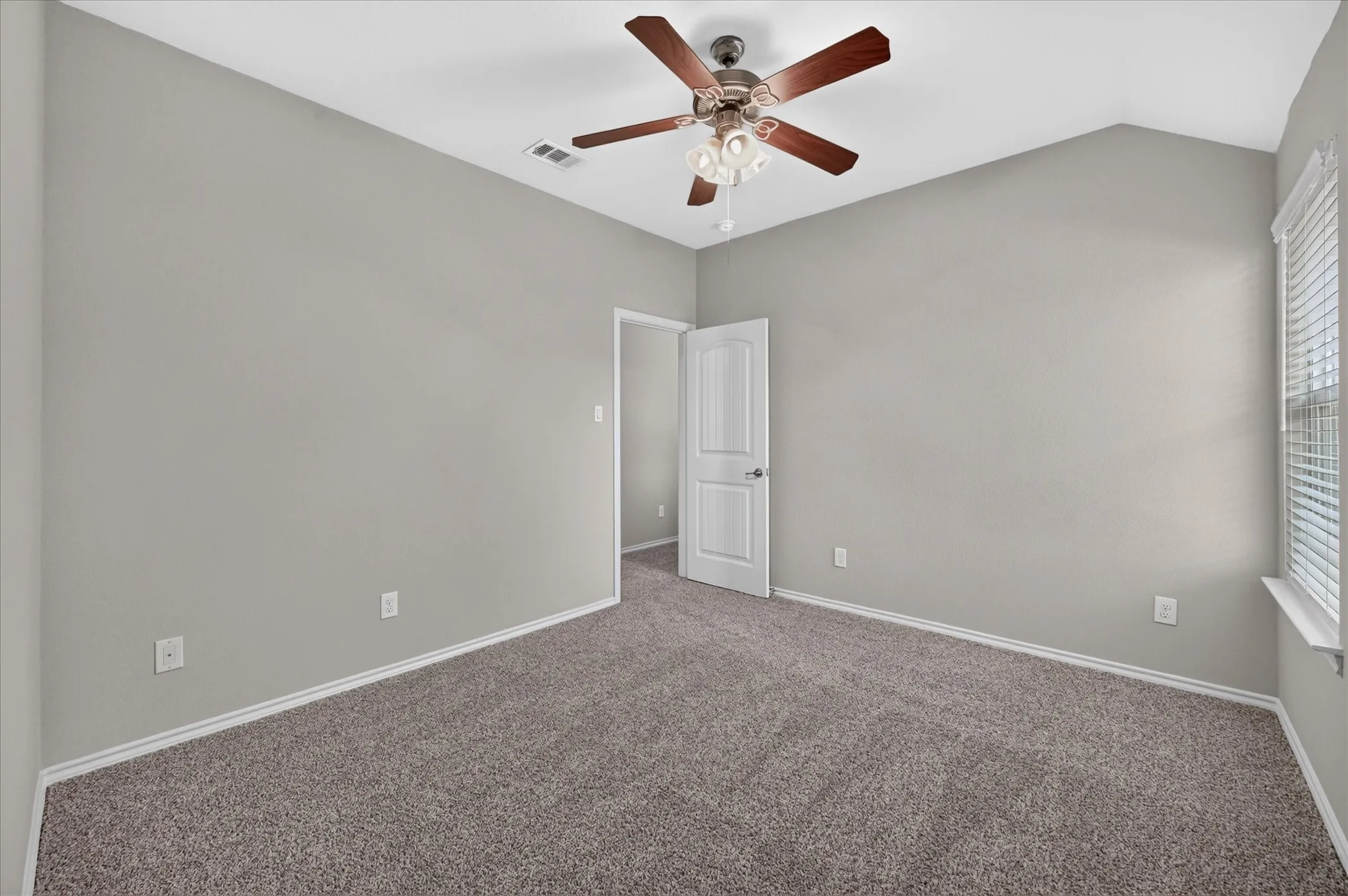 Vaulted ceiling room featuring neutral wall tones, carpet flooring, a ceiling fan with light fixture, and window with blinds