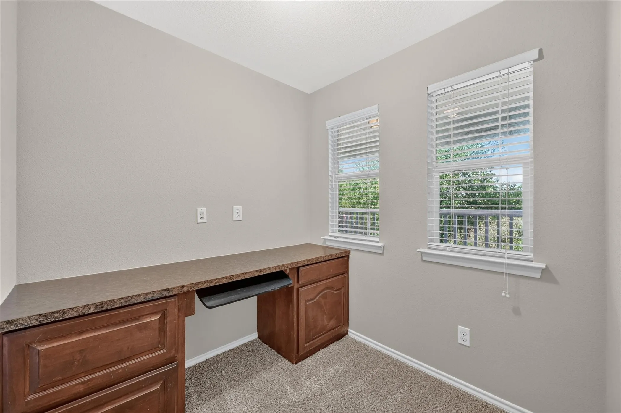 Built-in wood cabinetry with a stone-finish countertop, two windows with blinds, and neutral carpeting