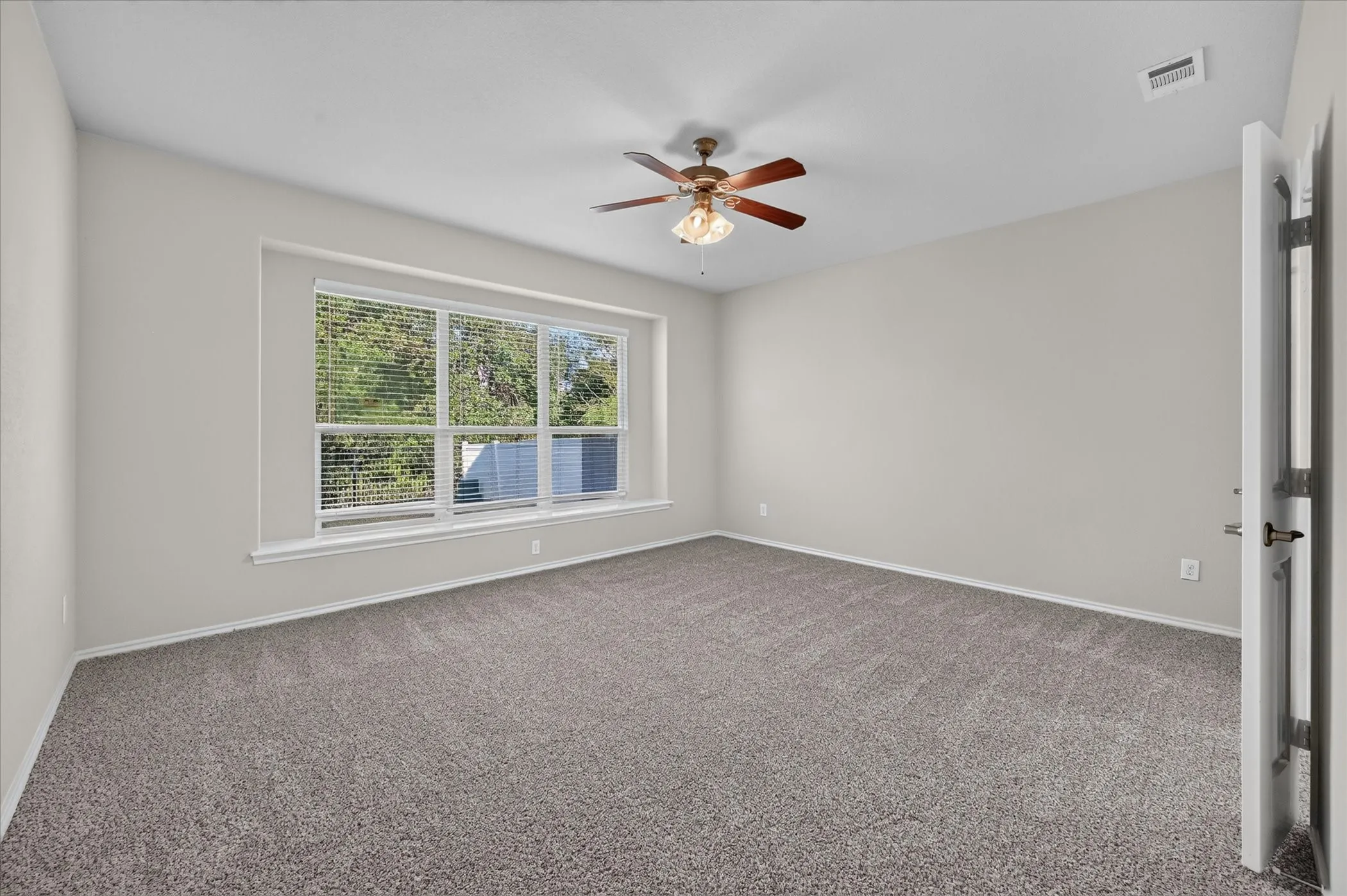 Recessed wall with multiple windows, neutral tone carpeting, and a ceiling fan with integrated lighting