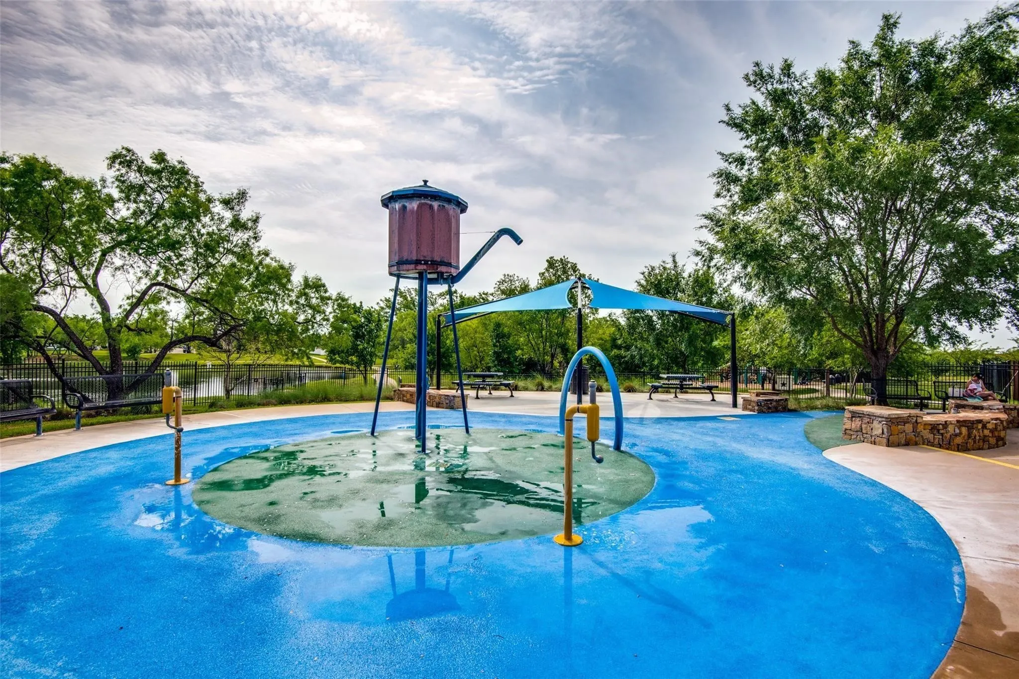 Splash pad with a water tower feature, a shade structure, and surrounding trees