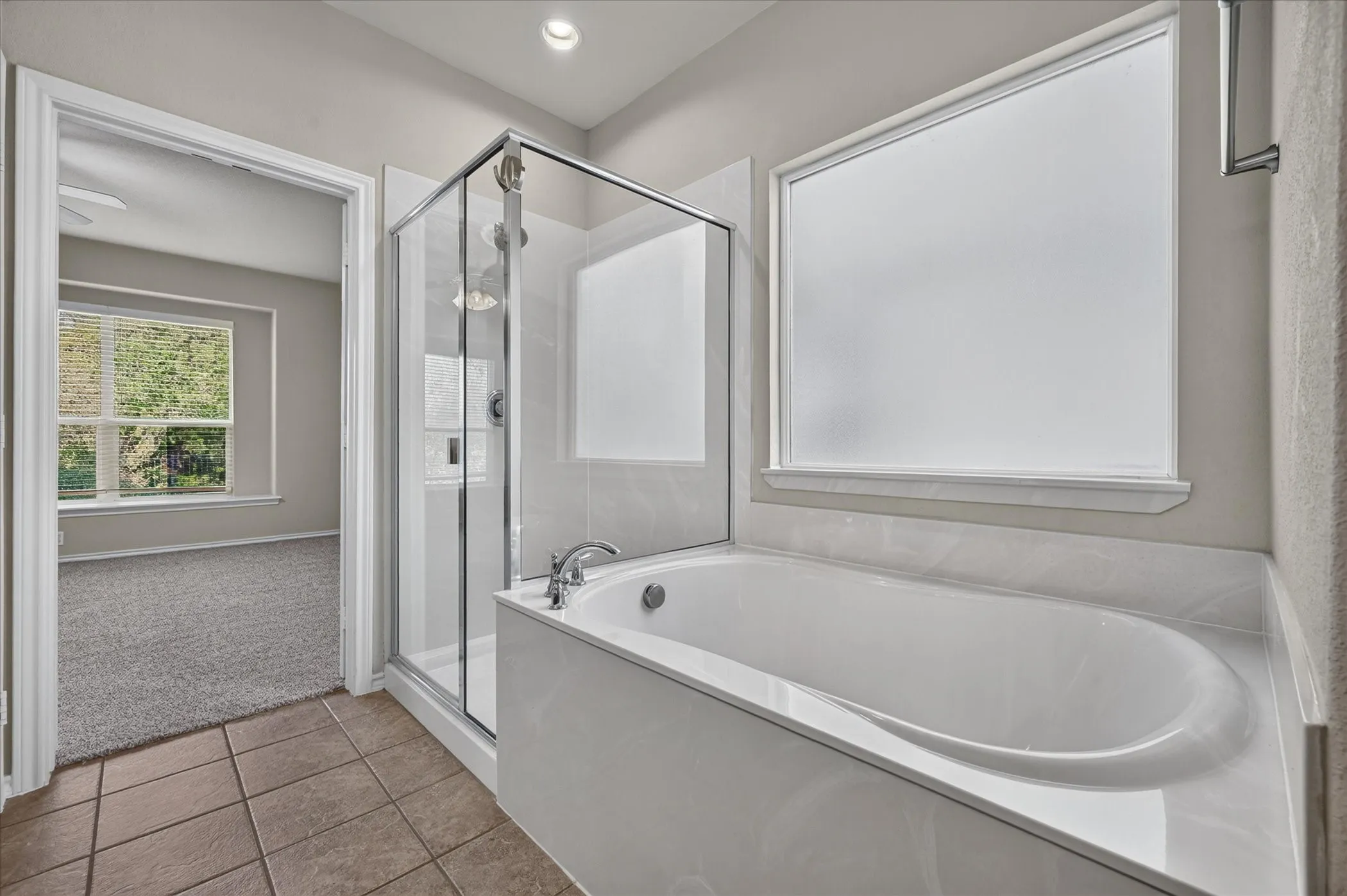 Built-in soaking tub, glass-enclosed shower, frosted window, recessed lighting, and tile flooring