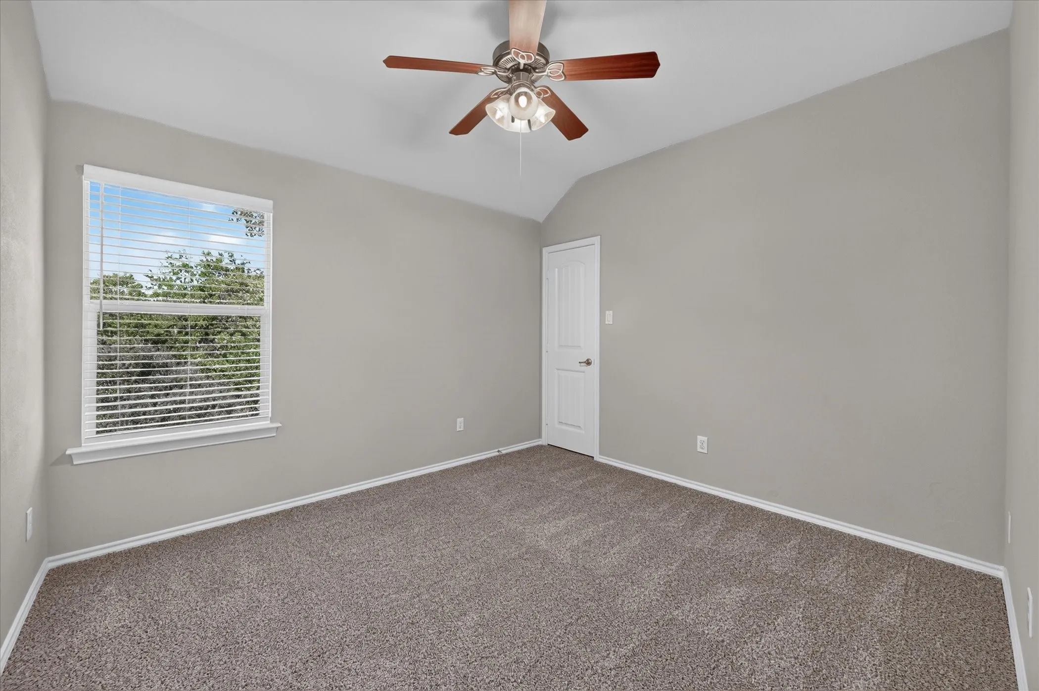 Vaulted ceiling, ceiling fan with light fixture, window with blinds, paneled door, and neutral carpeting