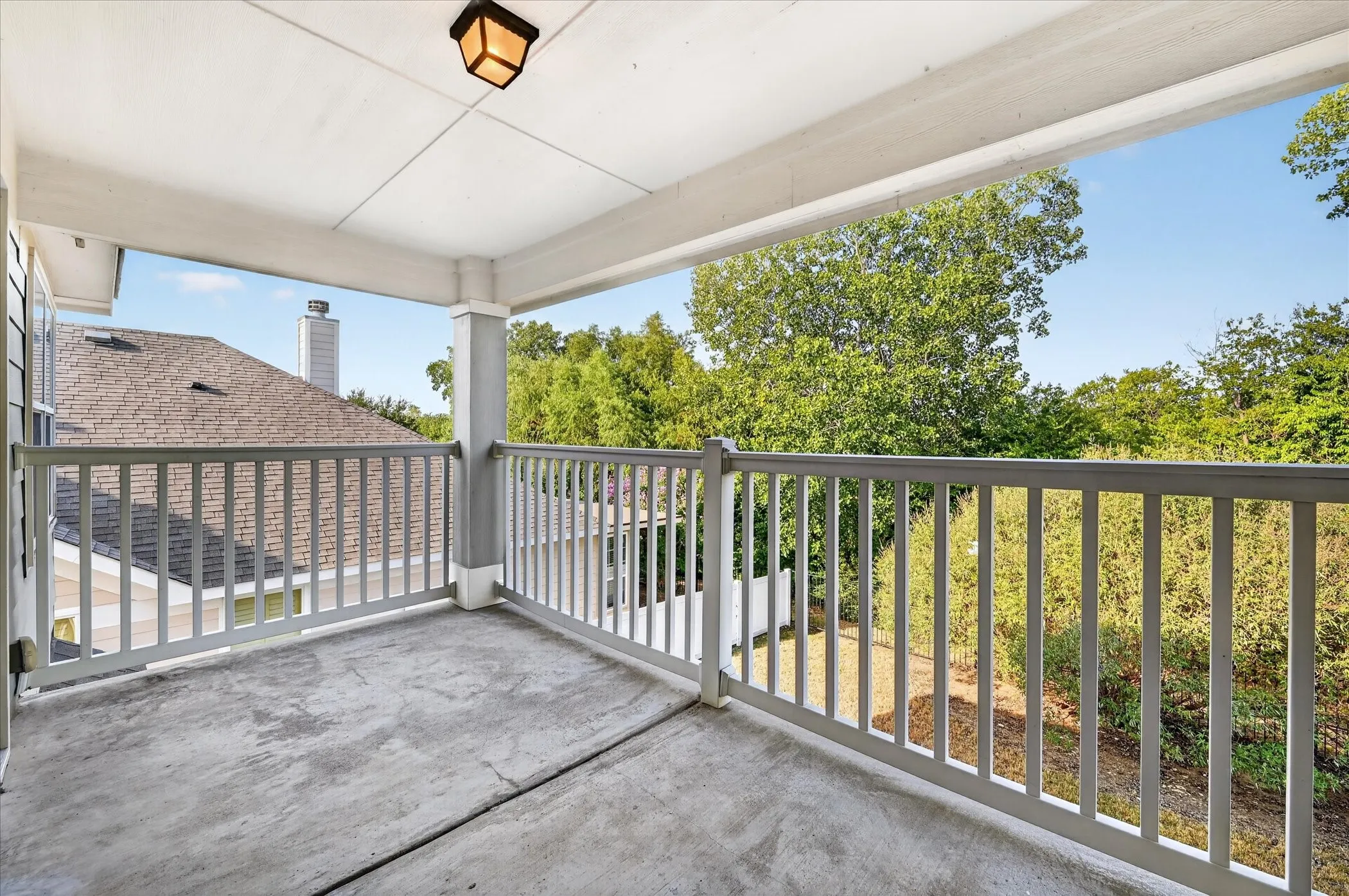Covered outdoor balcony featuring a concrete floor and painted wood railing