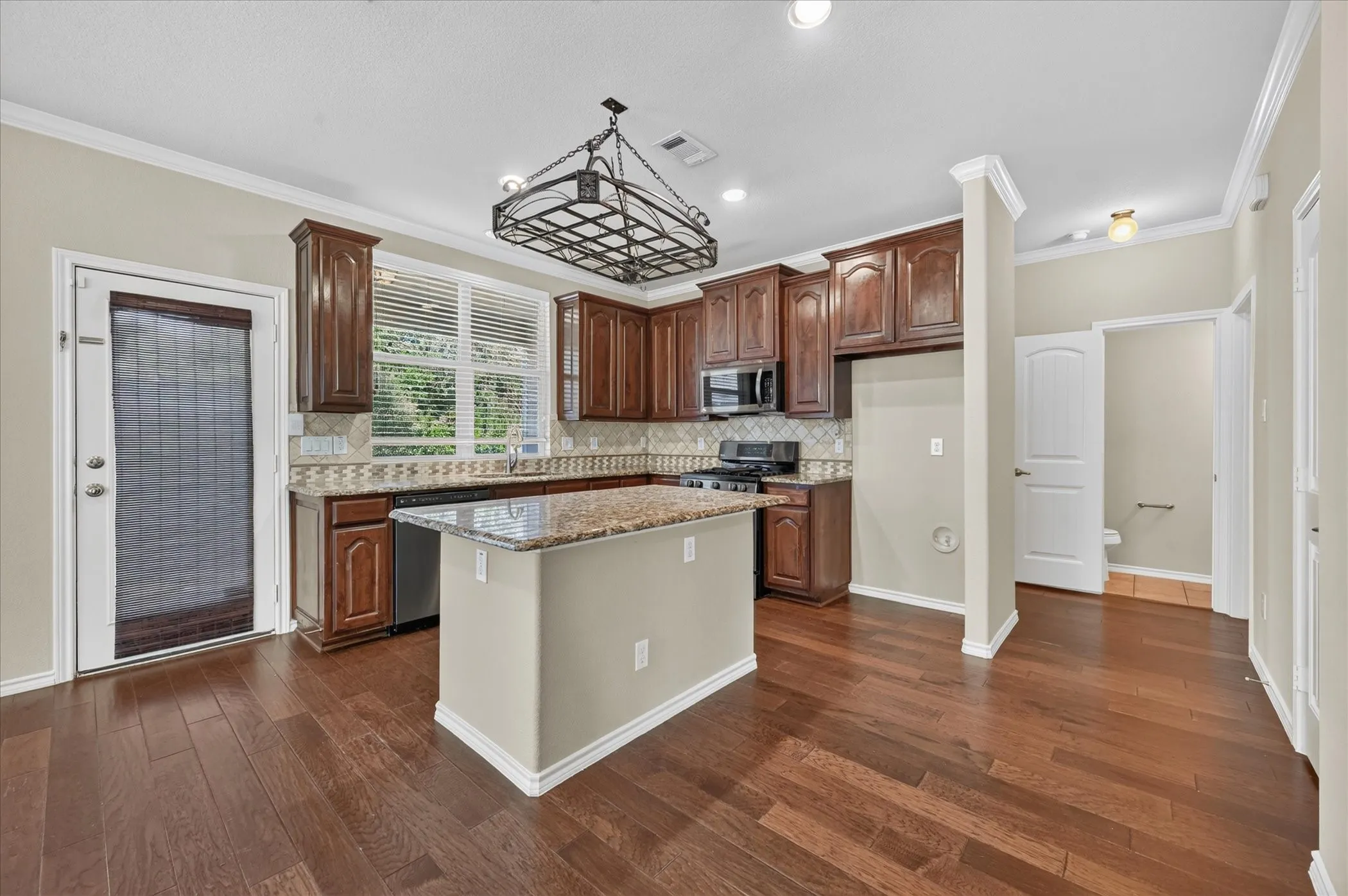 Kitchen featuring wood-finish flooring, dark wood cabinetry, a central island with a stone countertop, a tile backsplash, and stainless steel appliances