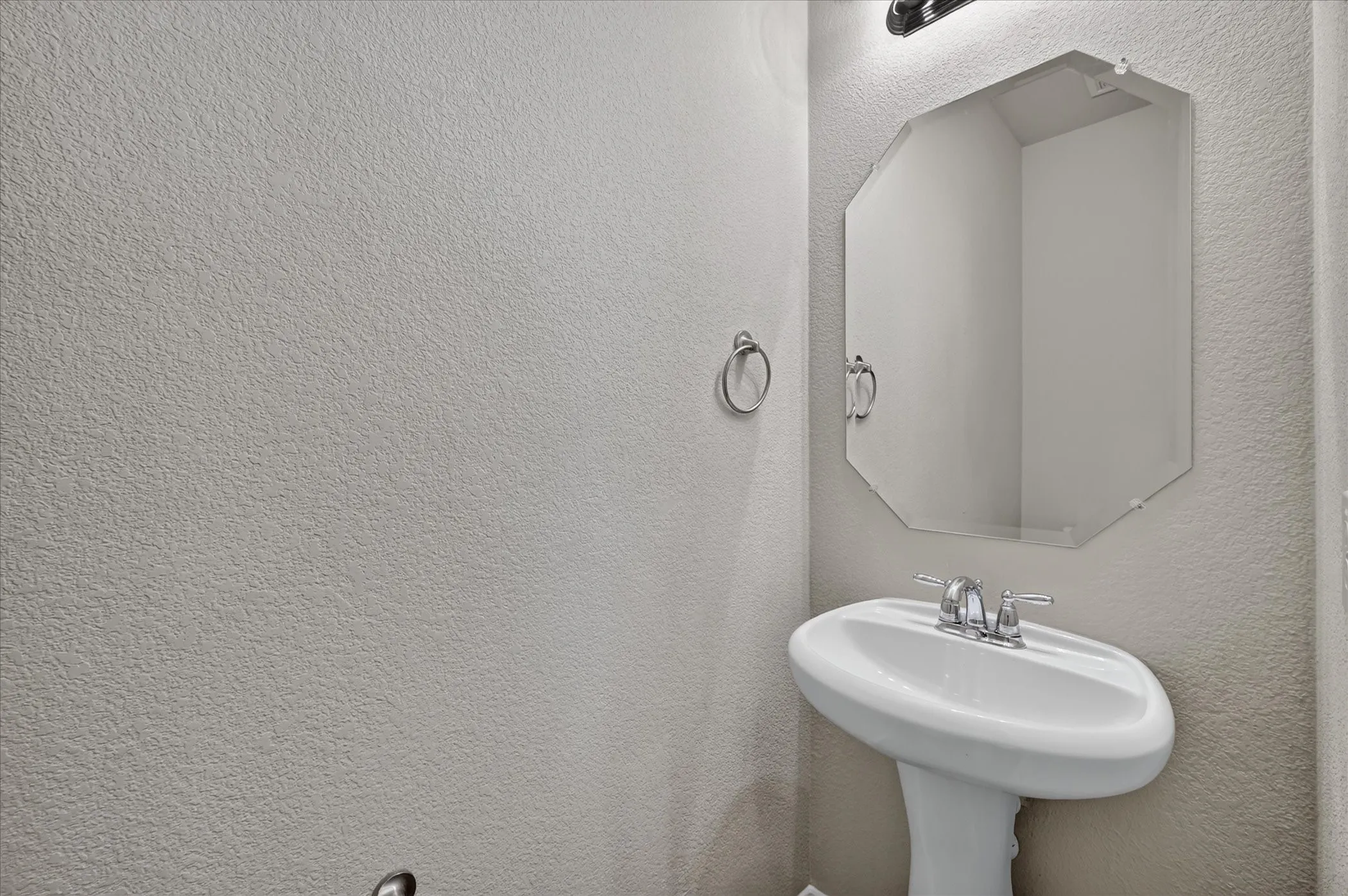 Pedestal sink with chrome hardware, octagonal frameless mirror, and overhead vanity lighting