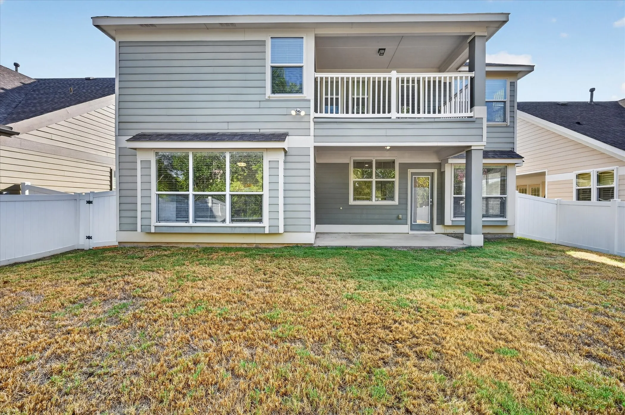 Rear elevation featuring multi-level outdoor living spaces, a covered patio, second-story balcony with white railing, and a bay window