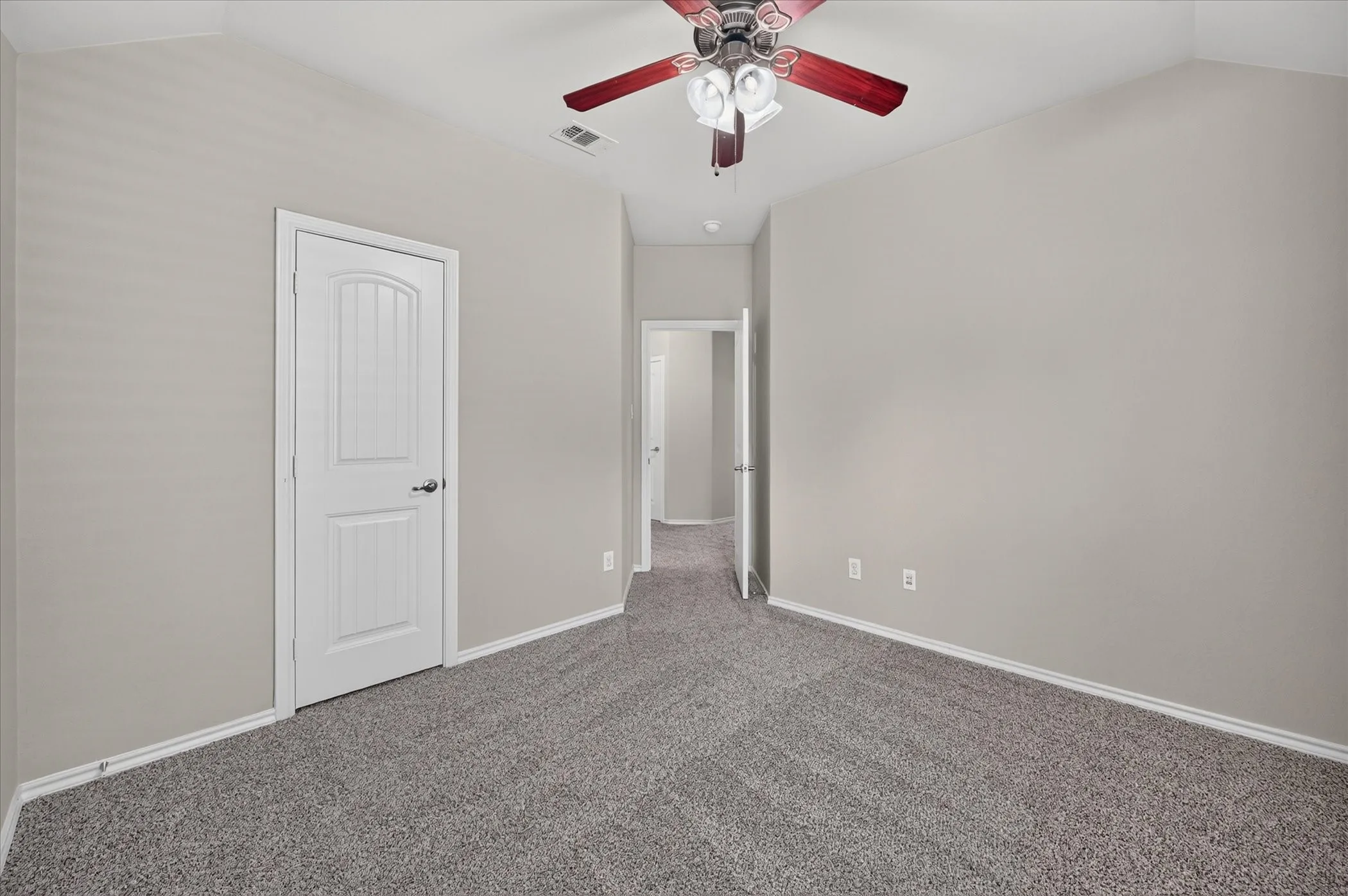 Vaulted ceiling with a ceiling fan, neutral wall paint, white paneled door, and textured carpet flooring