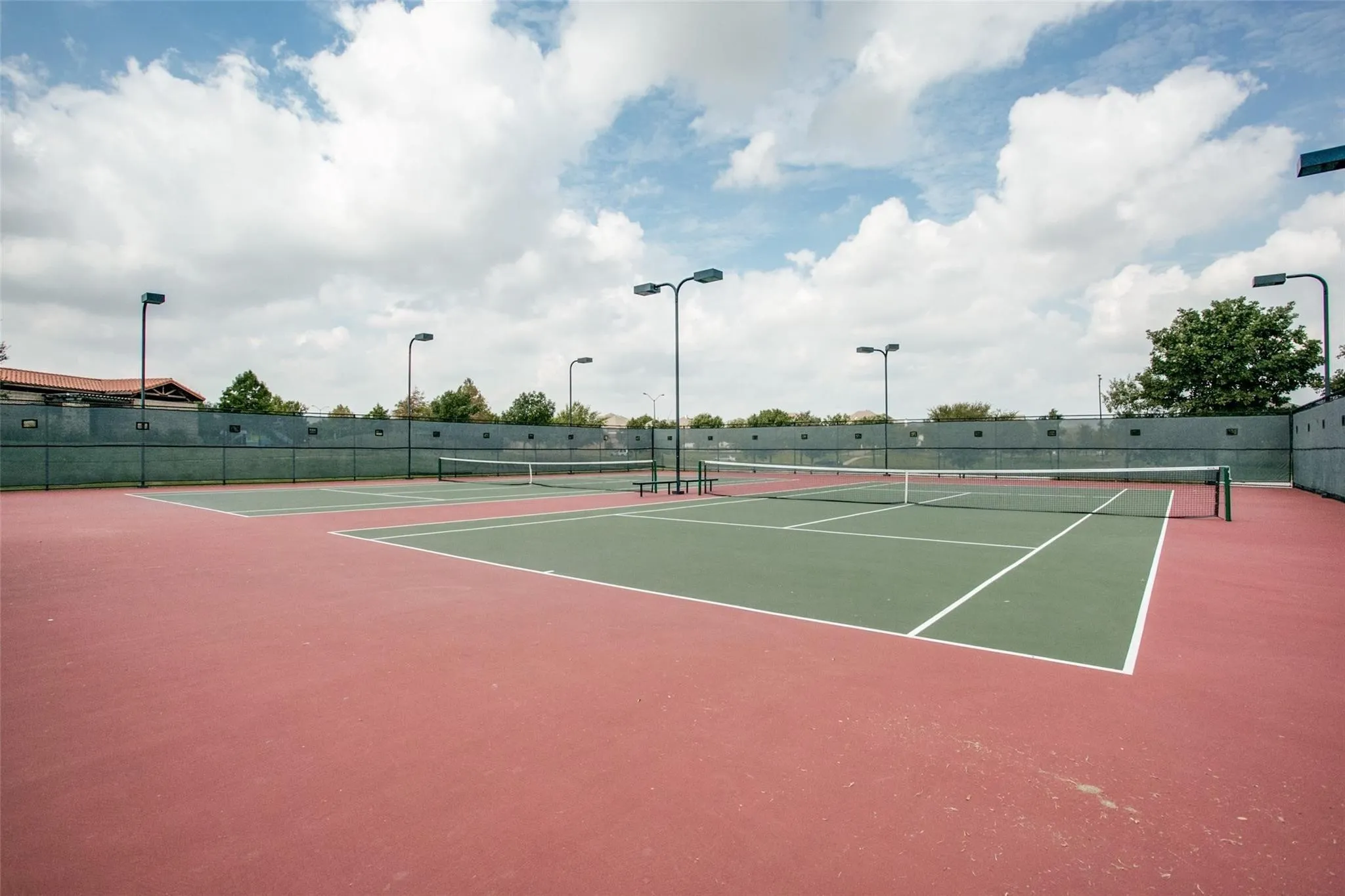 Two tennis courts with a red and green surface, white court lines, and chain-link fencing