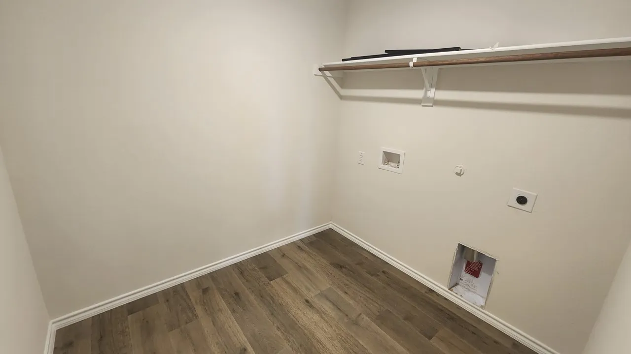 Dedicated laundry area featuring wood-finish flooring, light-toned walls, and a built-in shelving unit with a hanging rod