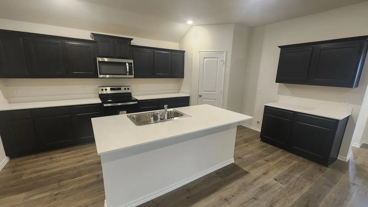 Kitchen featuring dark cabinetry, stainless steel appliances, a center island with an undermount sink, and wood-finish flooring