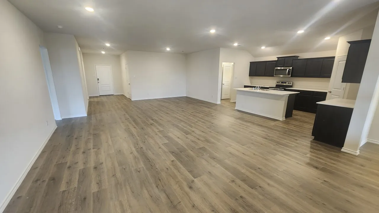 Open-concept kitchen and living area featuring wood-finish flooring, recessed lighting, white walls, dark cabinetry, and a kitchen island