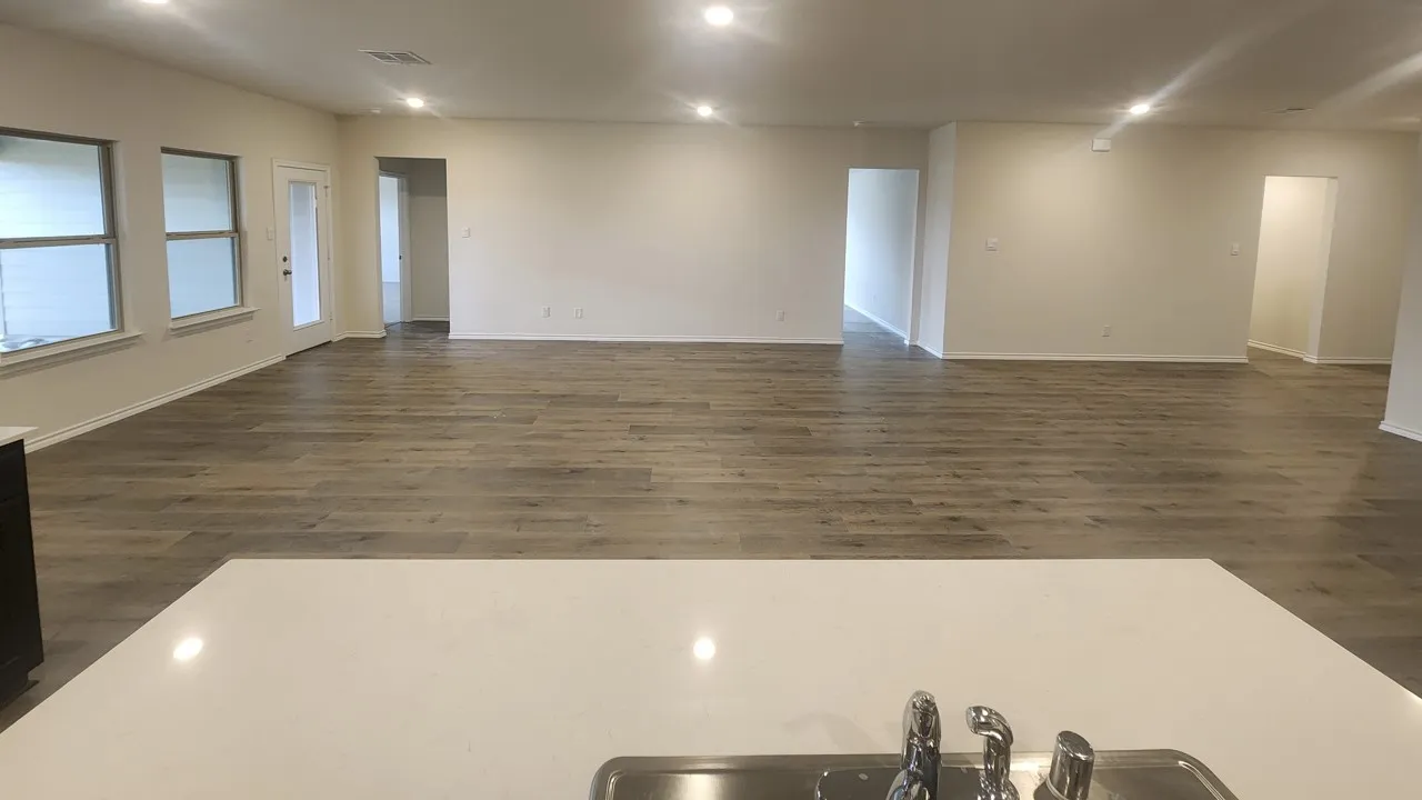 Expansive living area featuring wood-finish flooring, recessed lighting, multiple windows, a rear exterior door, and a kitchen island with an undermount sink