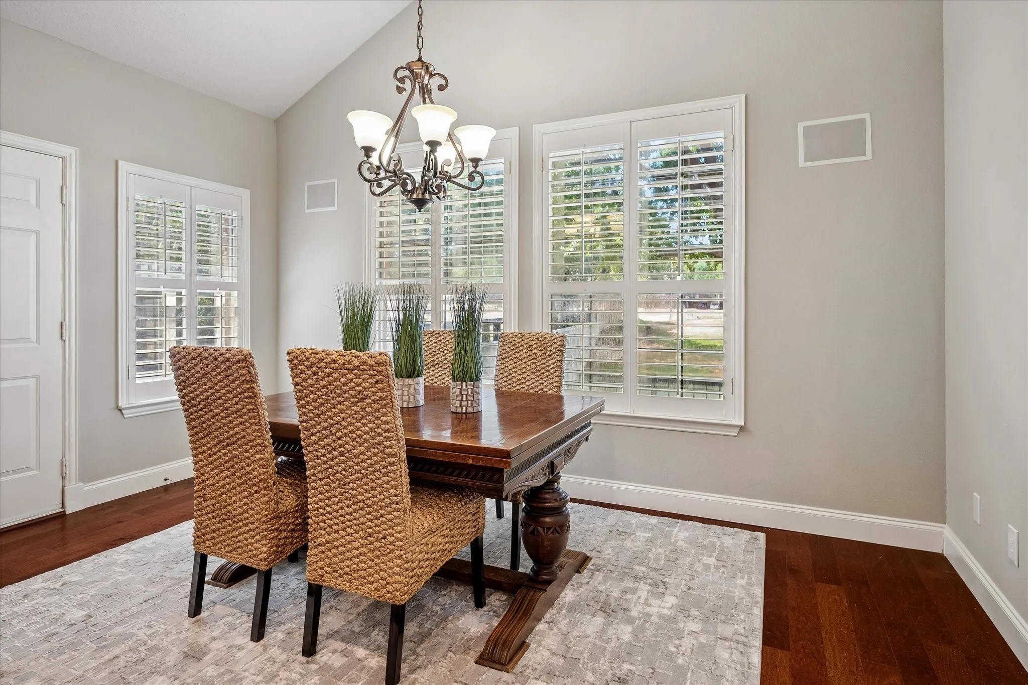 Vaulted ceiling with an ornate chandelier, rich wood-finish flooring, and white plantation shutters on multiple windows