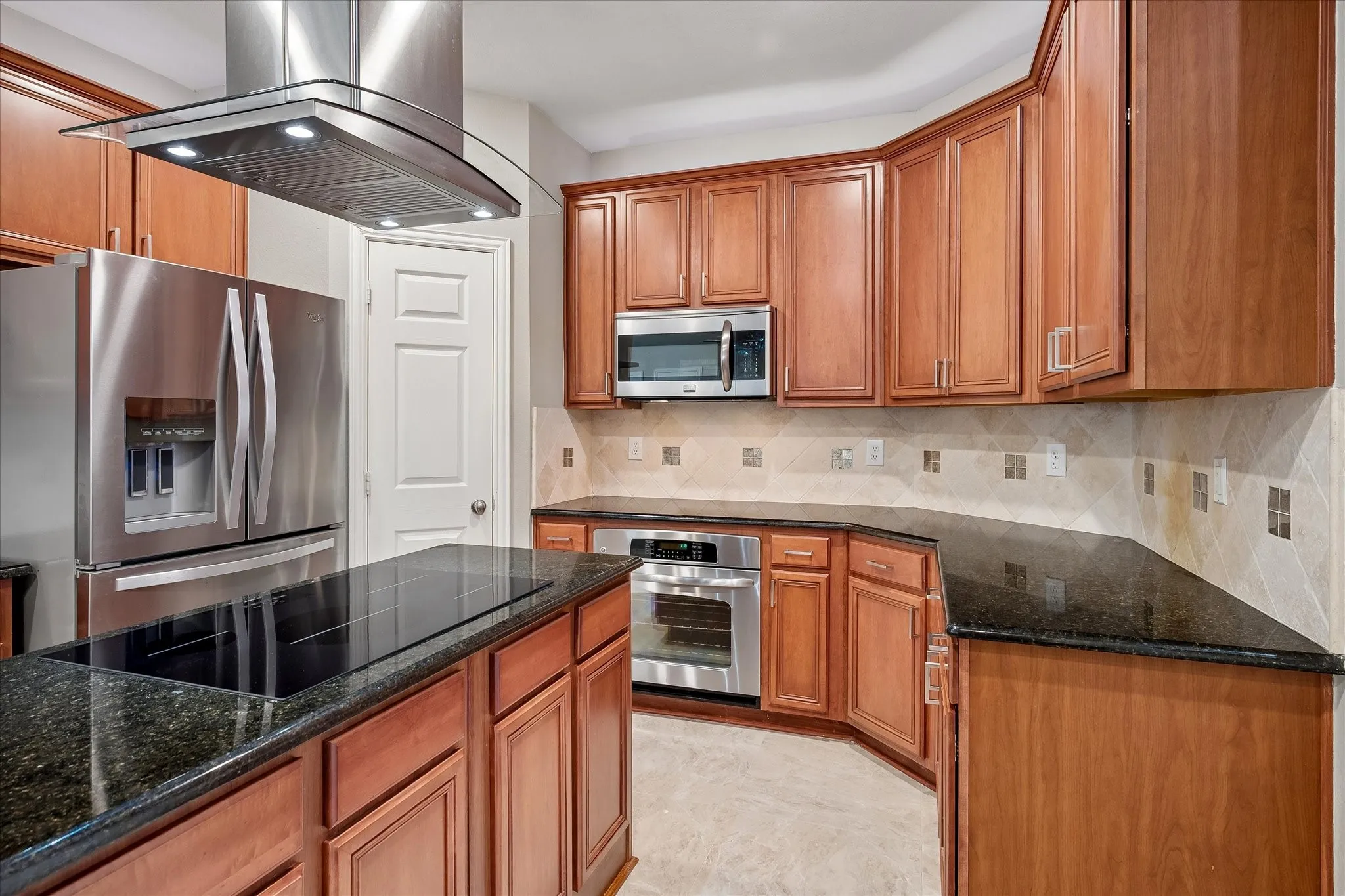 Kitchen featuring stainless steel appliances, wood-finish cabinetry, dark countertops, and a tiled backsplash