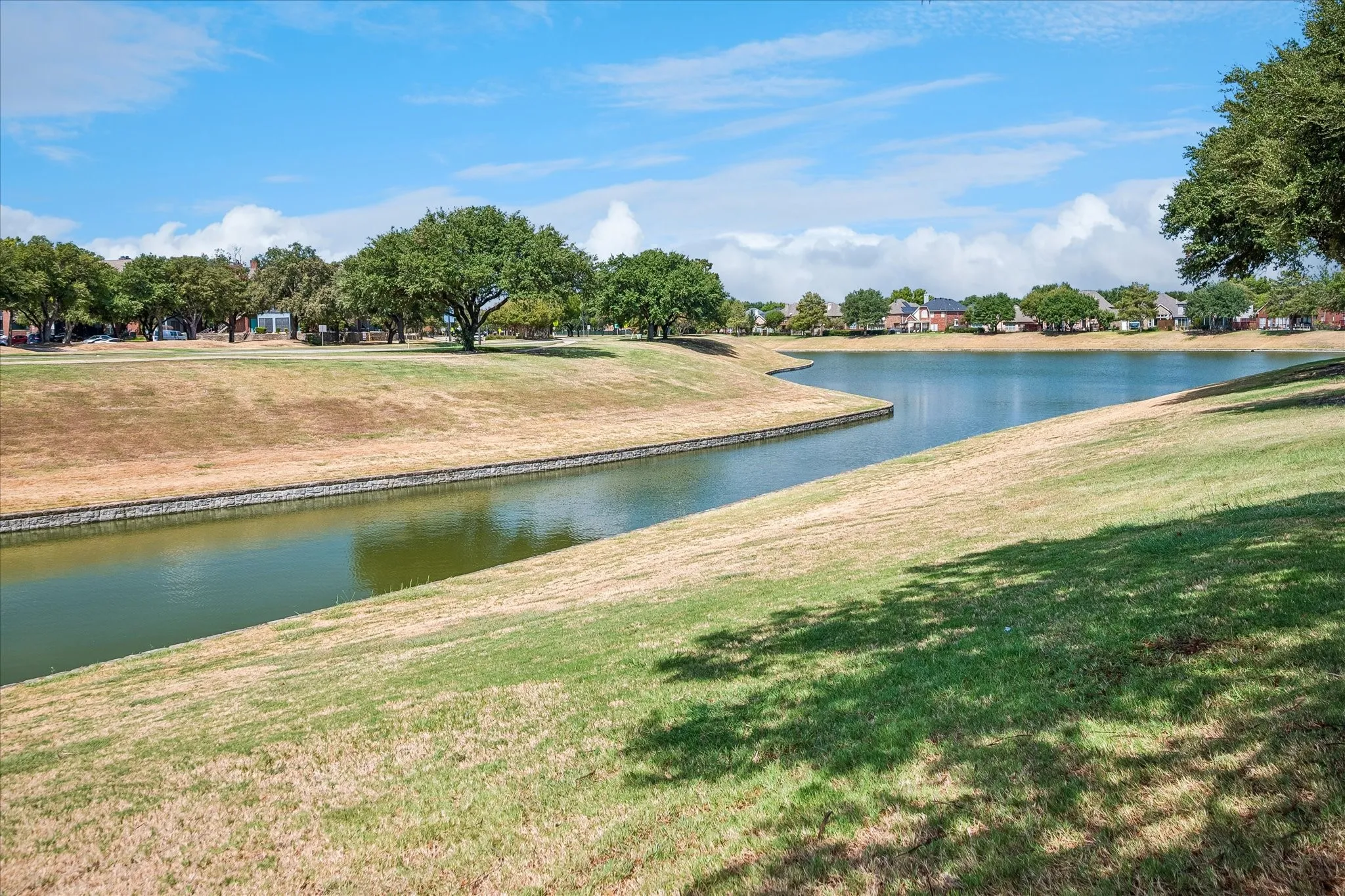 Expansive natural surroundings featuring a winding waterway, established trees, and gently sloping grassy banks