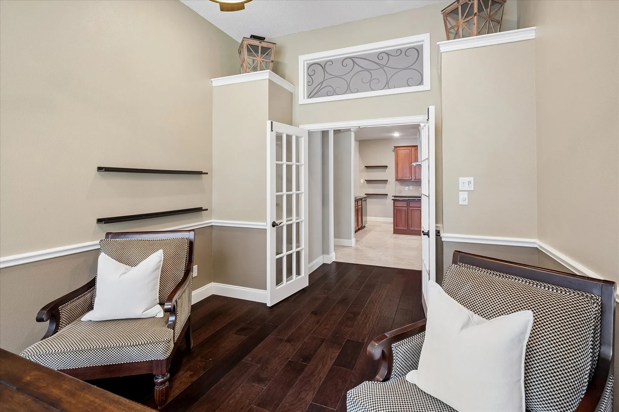Dark wood-finish flooring, two-tone wall treatment with chair rail, decorative wall shelving, double French doors, and vaulted ceilings