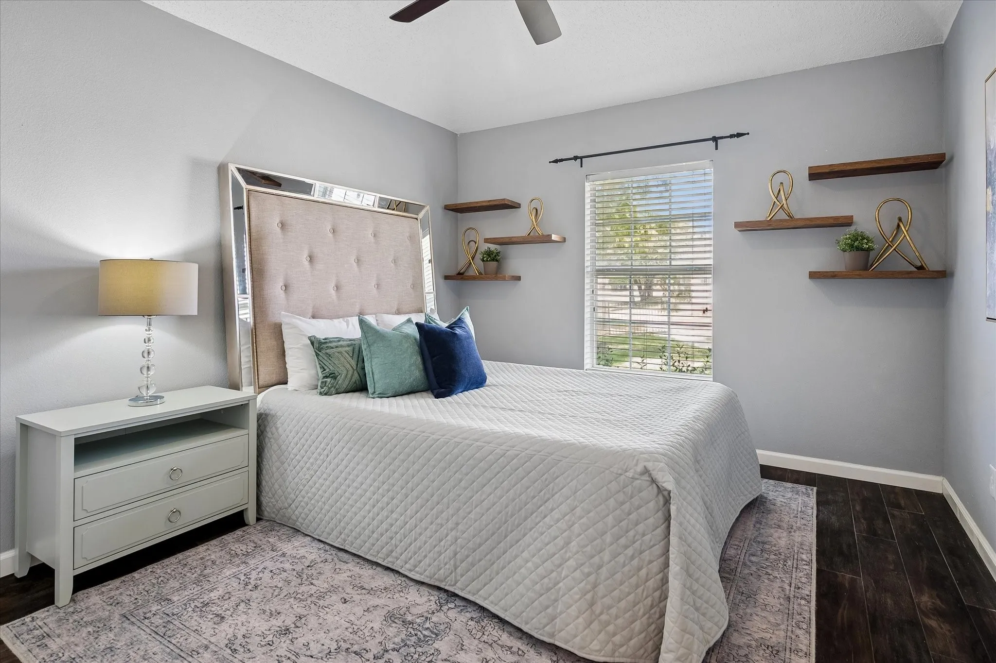 Wood-finish flooring, ceiling fan, window with blinds, and built-in floating shelves