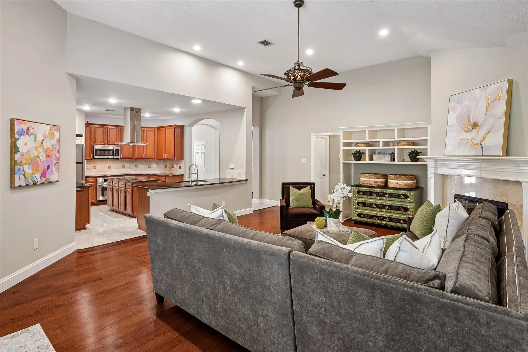 Vaulted ceilings with recessed lighting, wood-finish flooring, a built-in fireplace, and an open-concept kitchen with wood cabinetry and stainless steel appliances