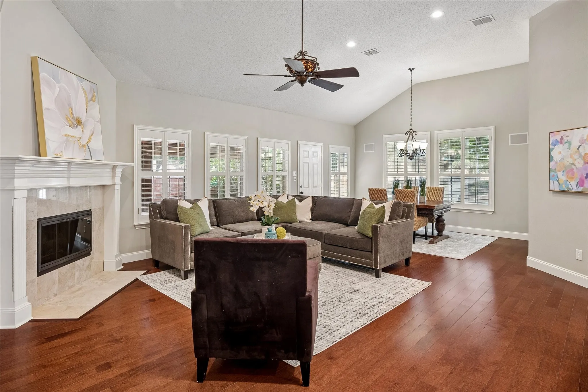 Vaulted ceilings with recessed lighting, wood-finish flooring, fireplace with a mantel, white plantation shutters, and a chandelier