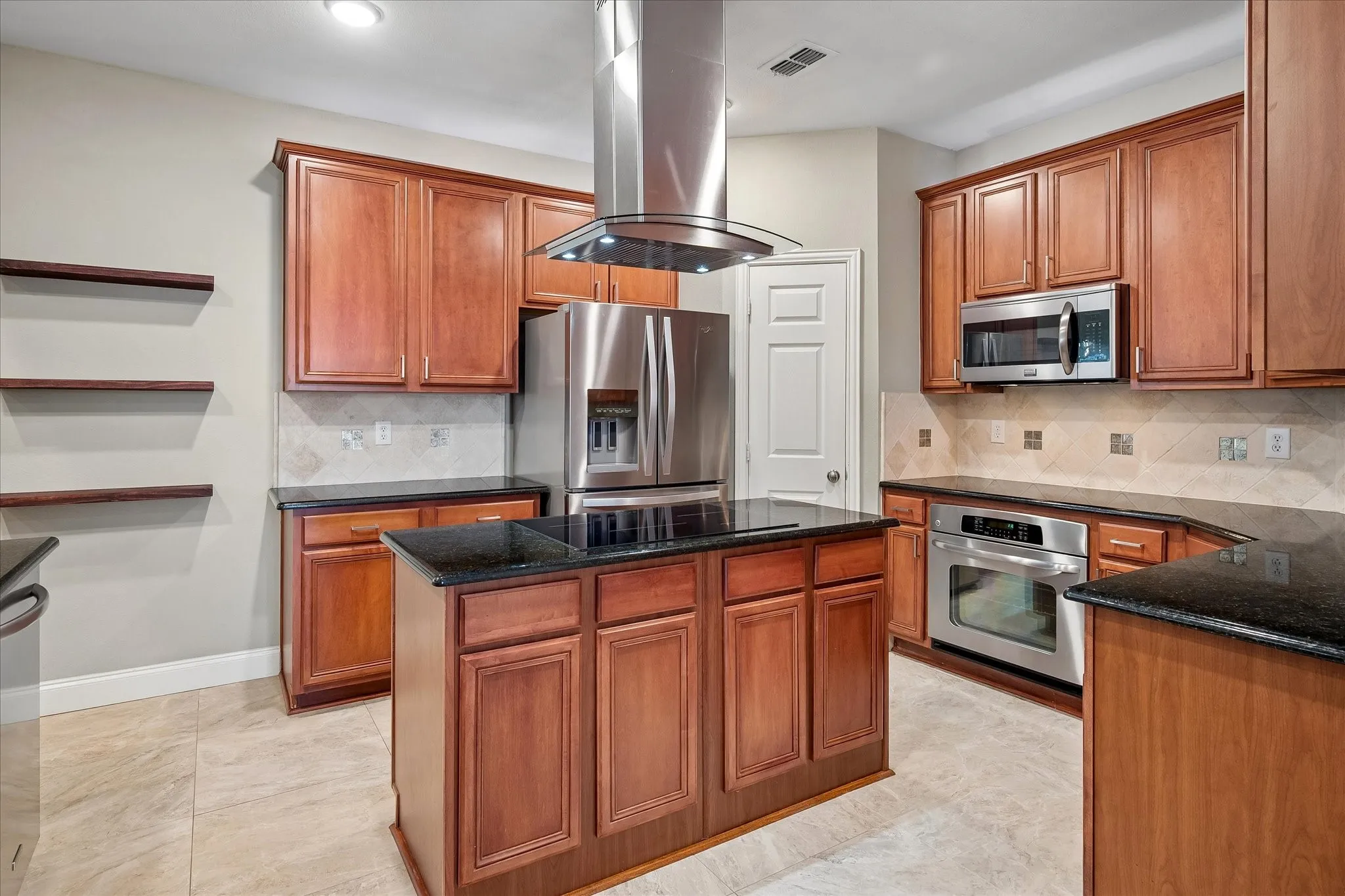 Kitchen featuring wood cabinetry, black countertops, stainless steel appliances, tile flooring, and a central island