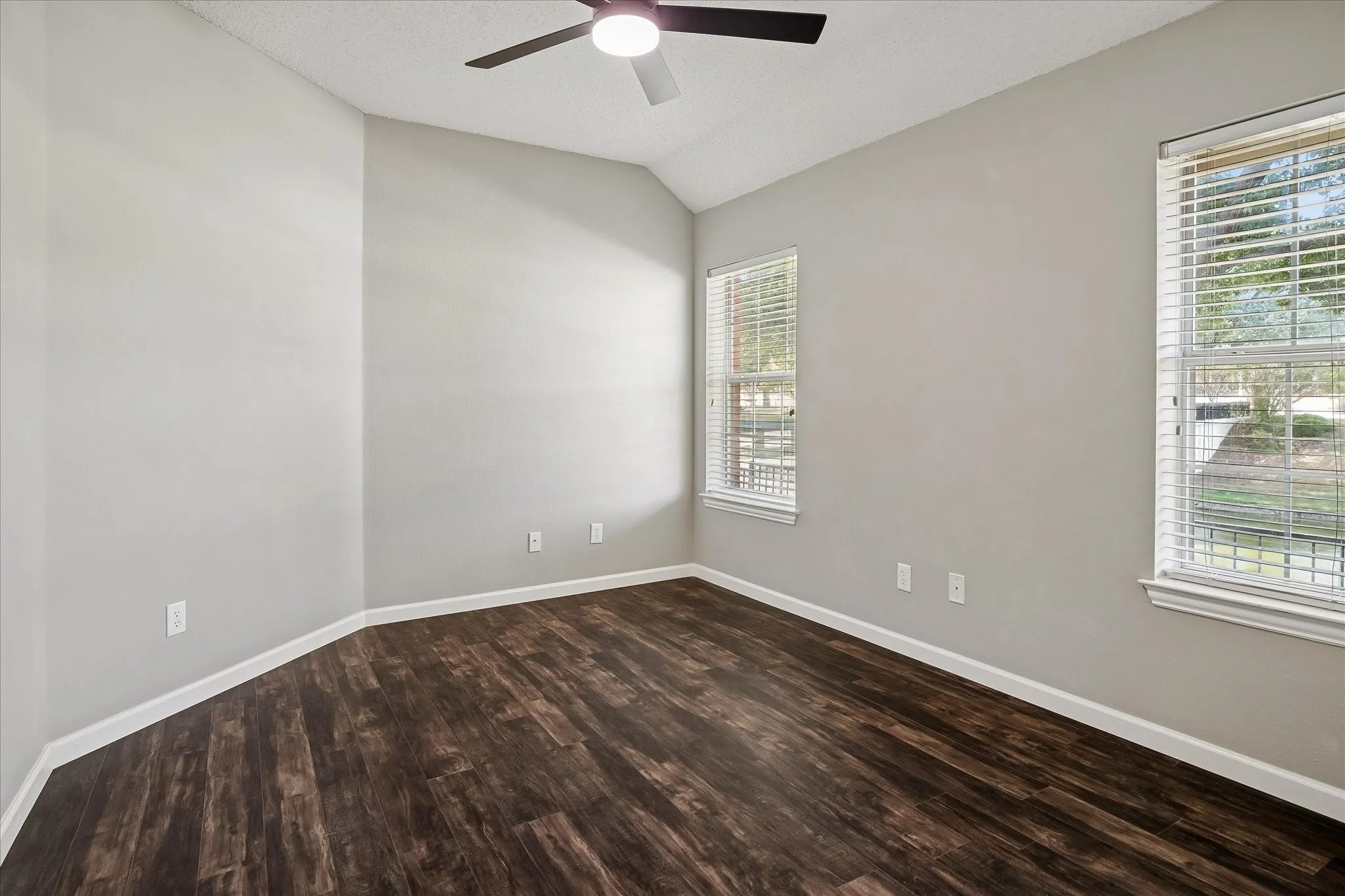 Vaulted ceiling with a ceiling fan, wood-finish flooring, and two windows with blinds