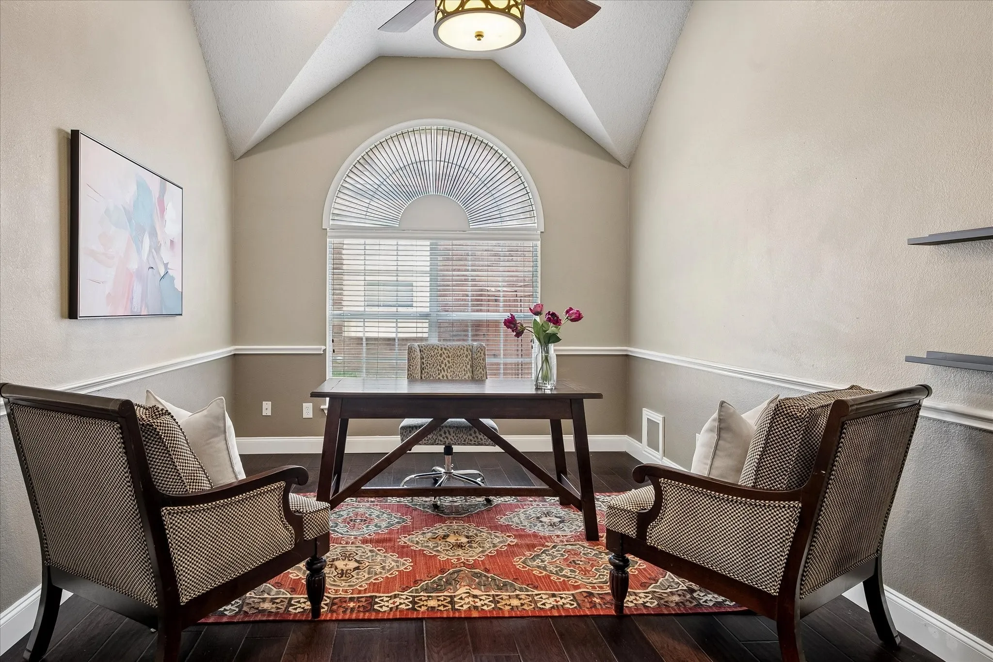 Vaulted ceiling with a ceiling fan, decorative window with an arched transom, dark wood-finish flooring, and chair rail molding