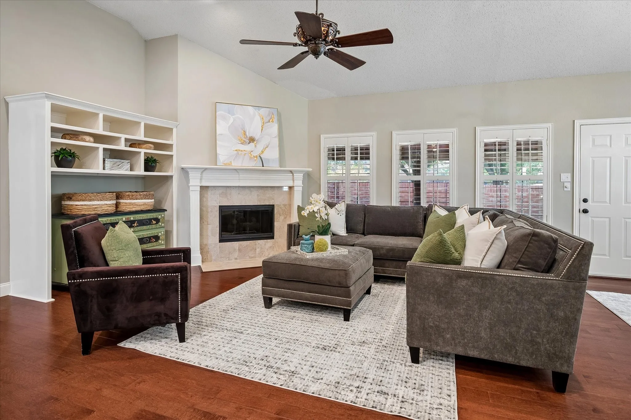 Vaulted ceiling, wood-finish flooring, built-in shelving, fireplace with stone surround, and ceiling fan