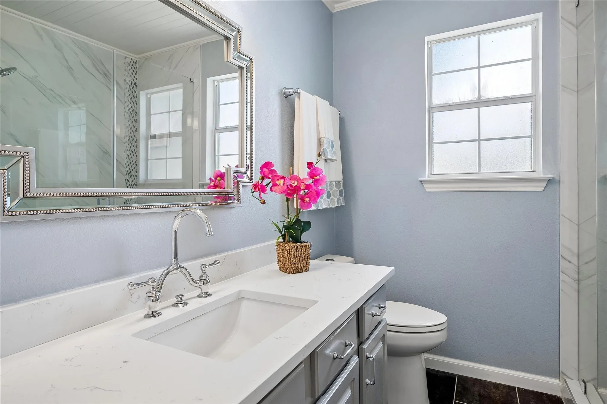 White countertop with integrated sink, chrome faucet, decorative framed mirror, and a frosted glass window
