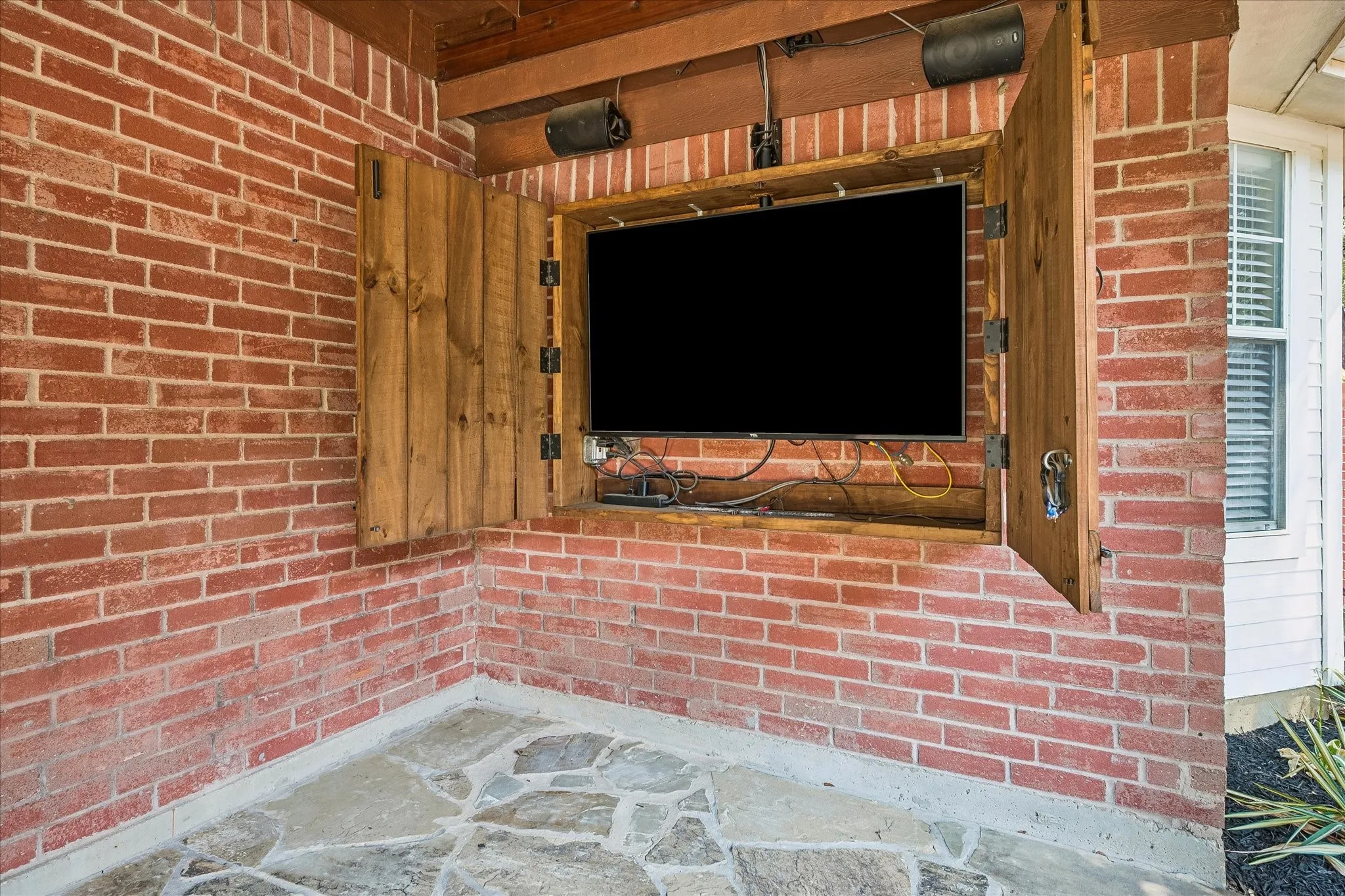 Brick wall construction with a built-in media cabinet featuring wood-finish doors, integrated television, and overhead speakers