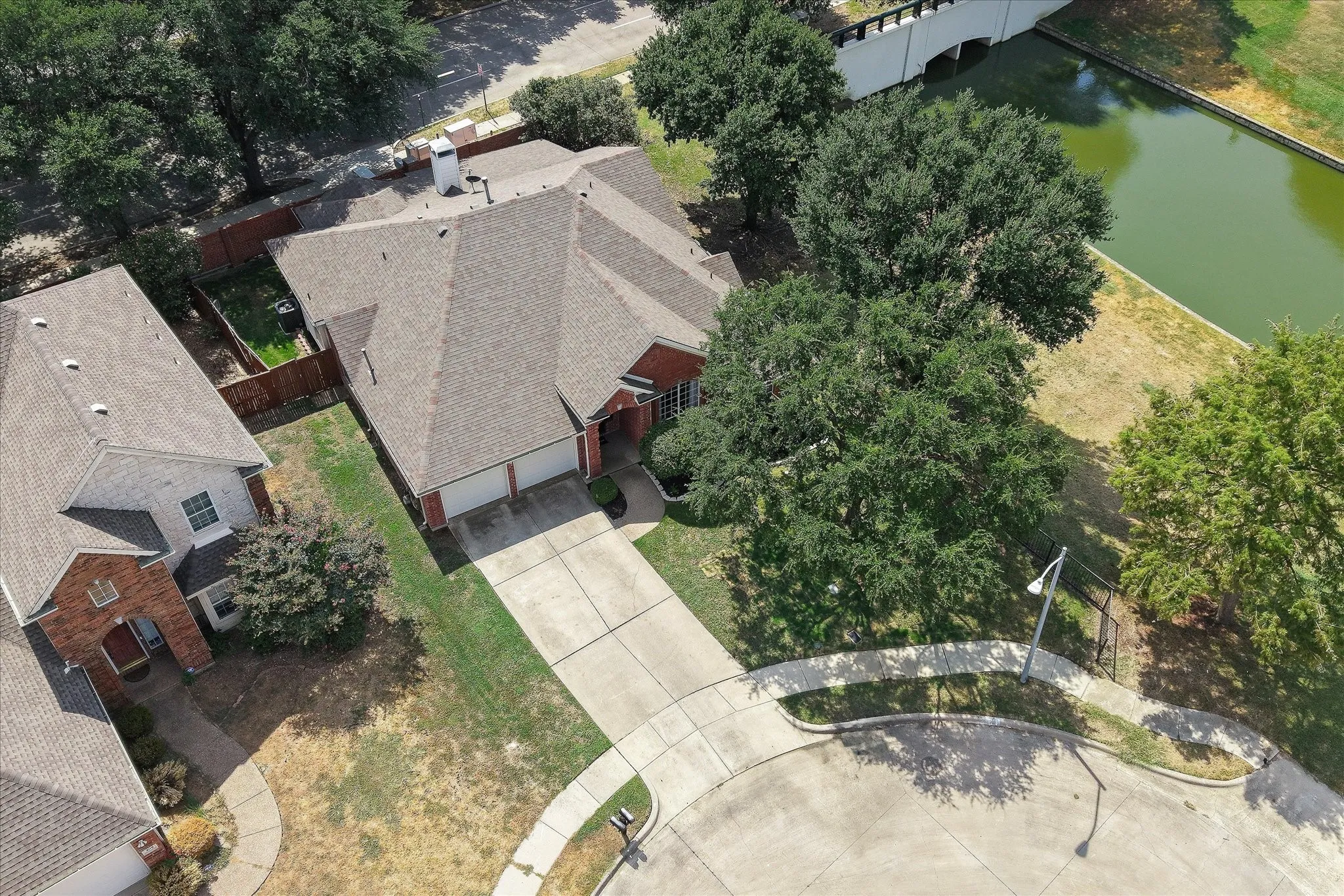 Red brick exterior with a two-car garage, mature trees, and a paved driveway