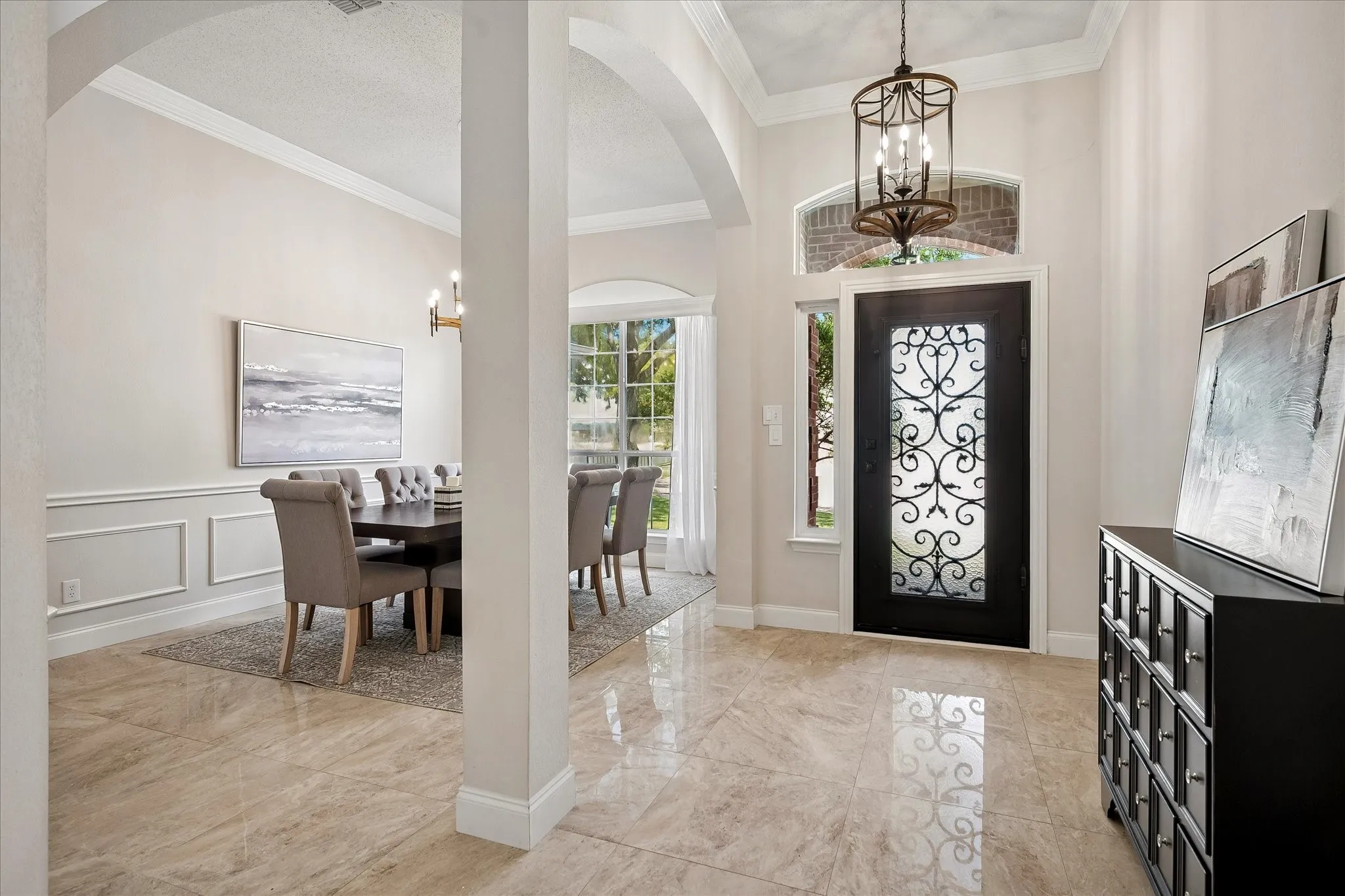 Foyer featuring large format tile flooring, arched entryways, decorative iron front door, and a tray ceiling with an ornate chandelier