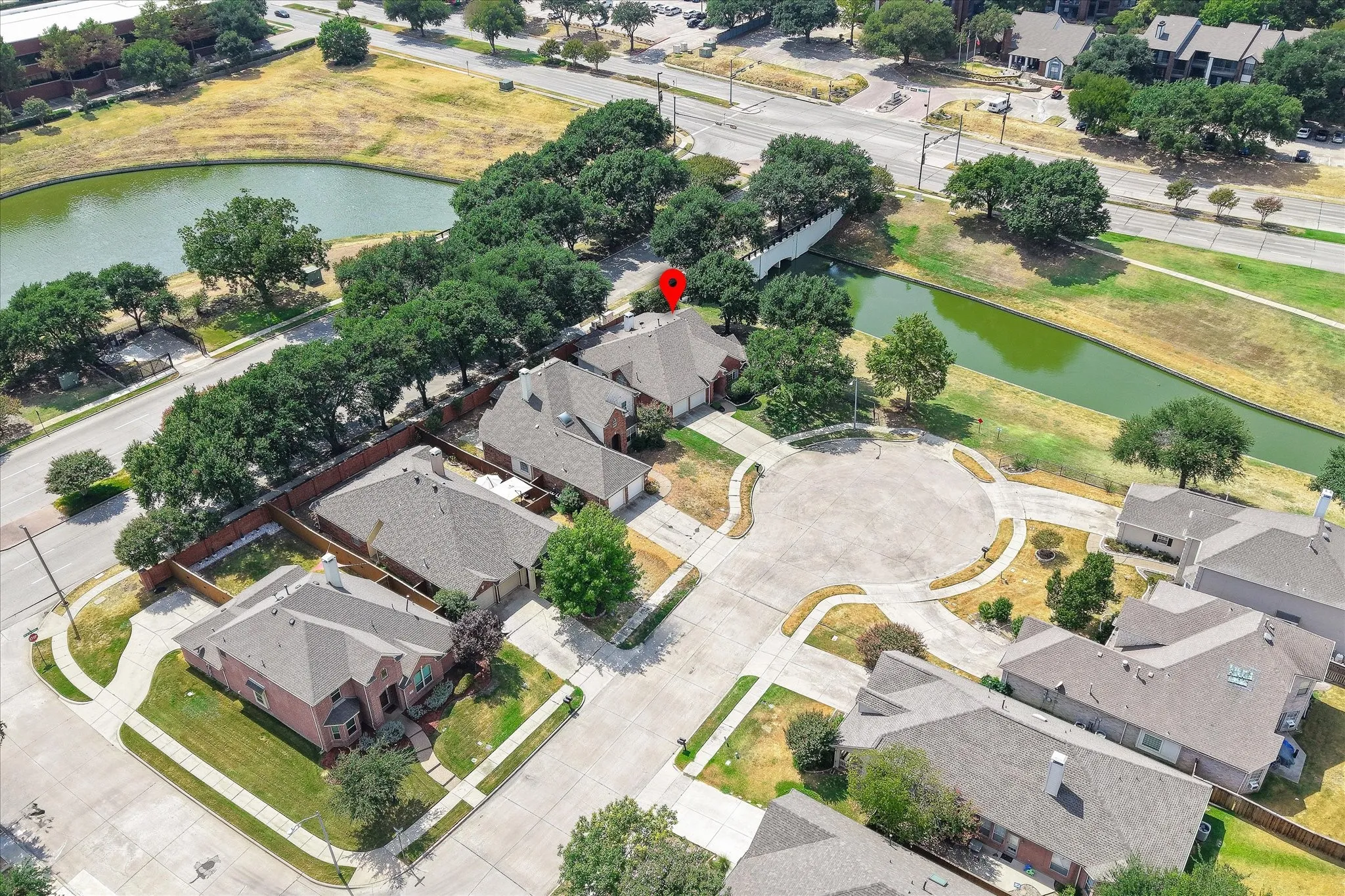 Aerial perspective featuring a residential cul-de-sac, adjacent to a park-like area with a pond and a waterway