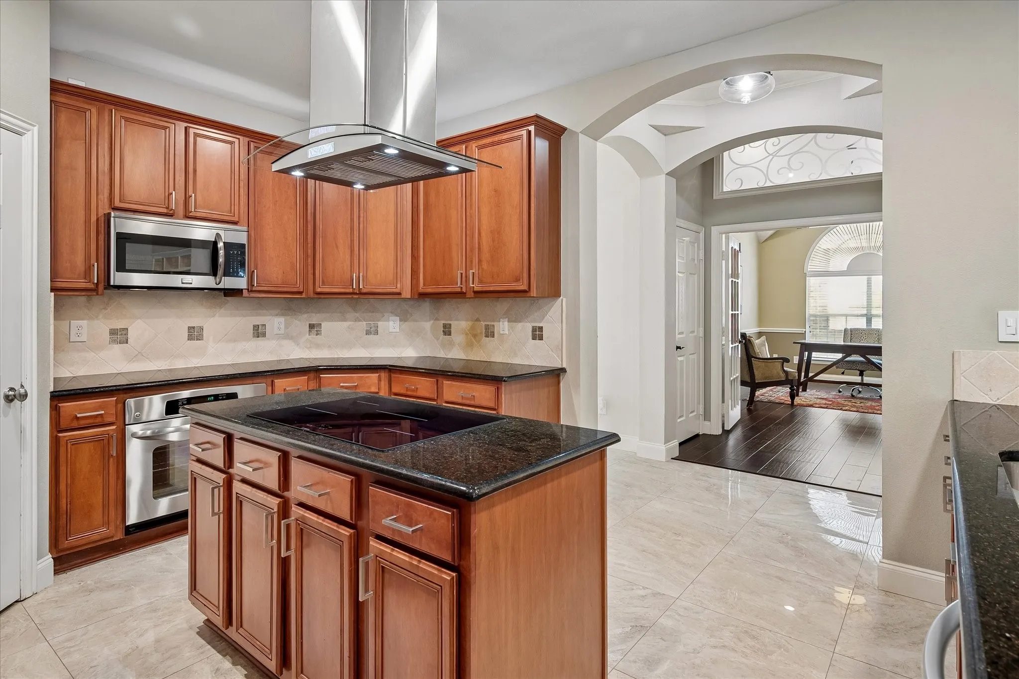 Kitchen featuring wood cabinetry, stainless steel appliances, a center island with cooktop, and granite countertops