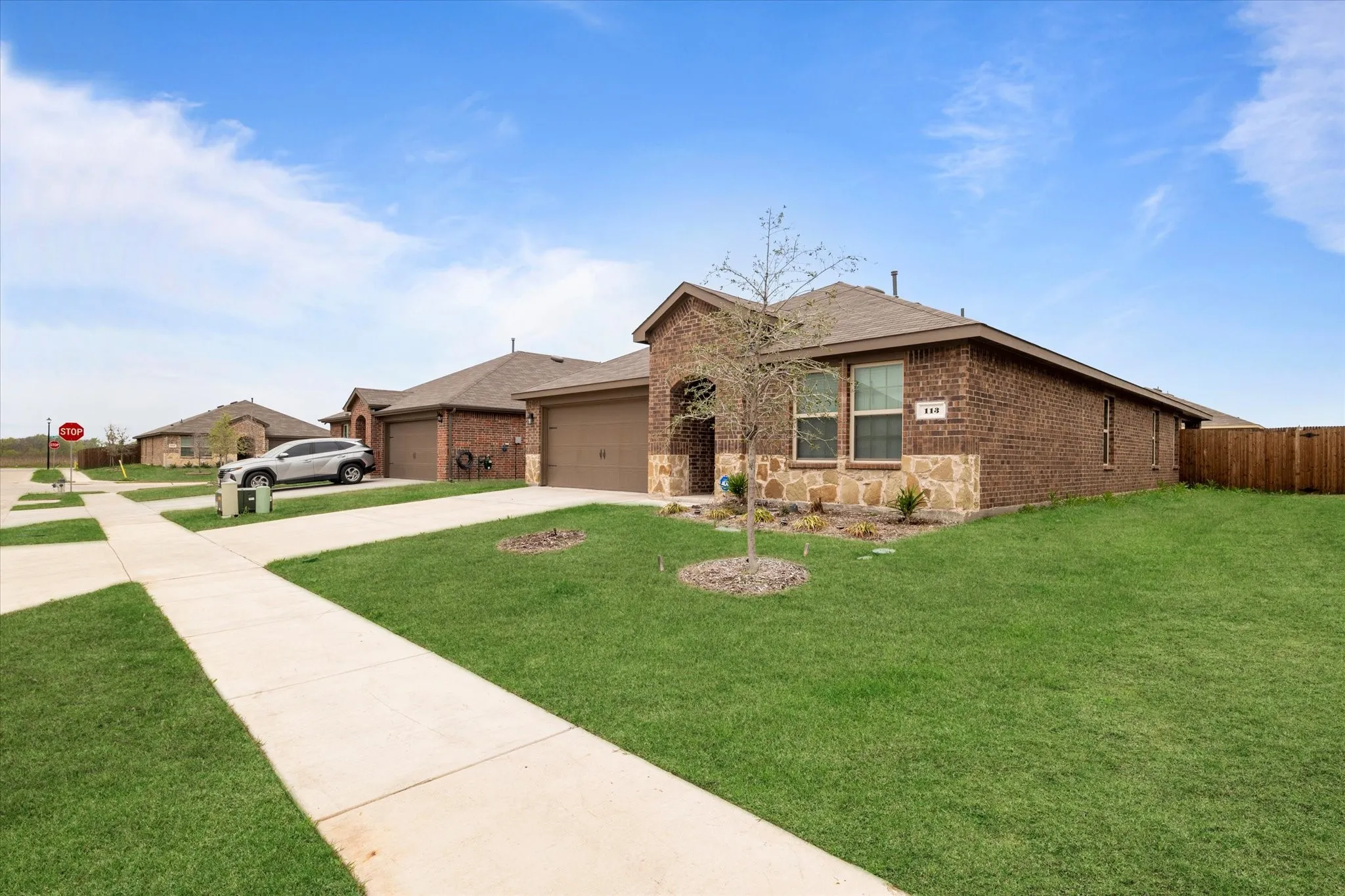 Ranch-style home with brick siding, driveway, an attached garage, a front yard, and a shingled roof