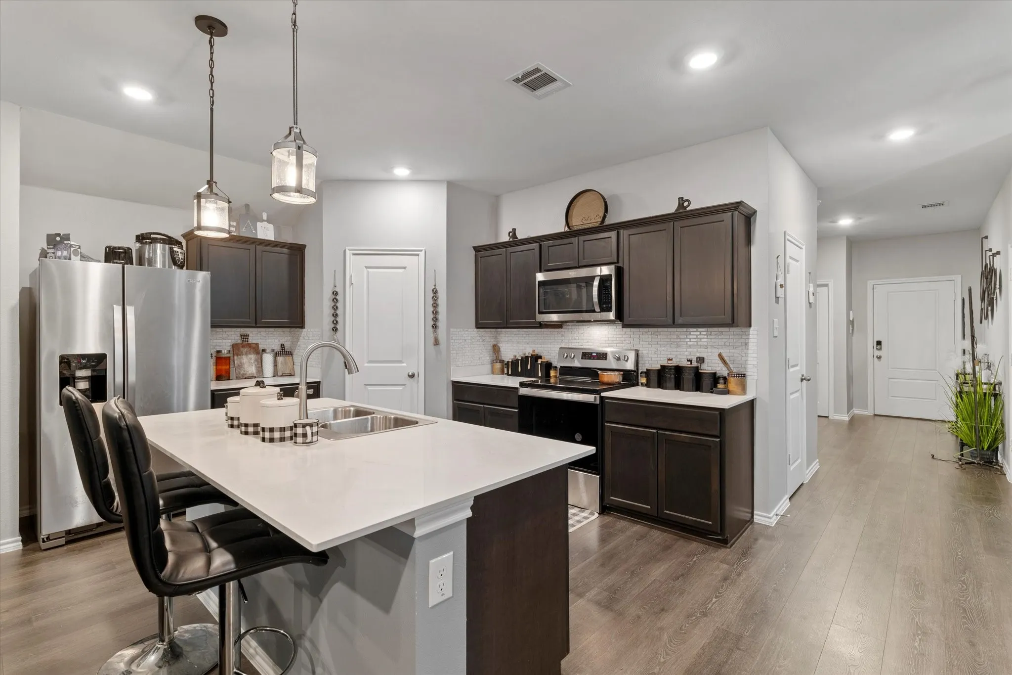 Kitchen featuring dark brown cabinetry, a kitchen bar, appliances with stainless steel finishes, tasteful backsplash, and decorative light fixtures