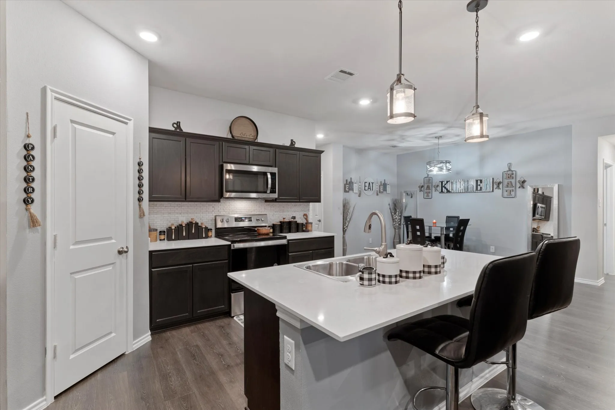 Kitchen featuring decorative backsplash, appliances with stainless steel finishes, dark wood finished floors, a kitchen bar, and a kitchen island with sink