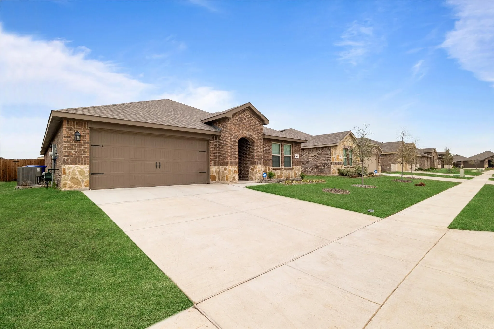 Ranch-style house featuring a shingled roof, brick siding, driveway, stone siding, and a front lawn