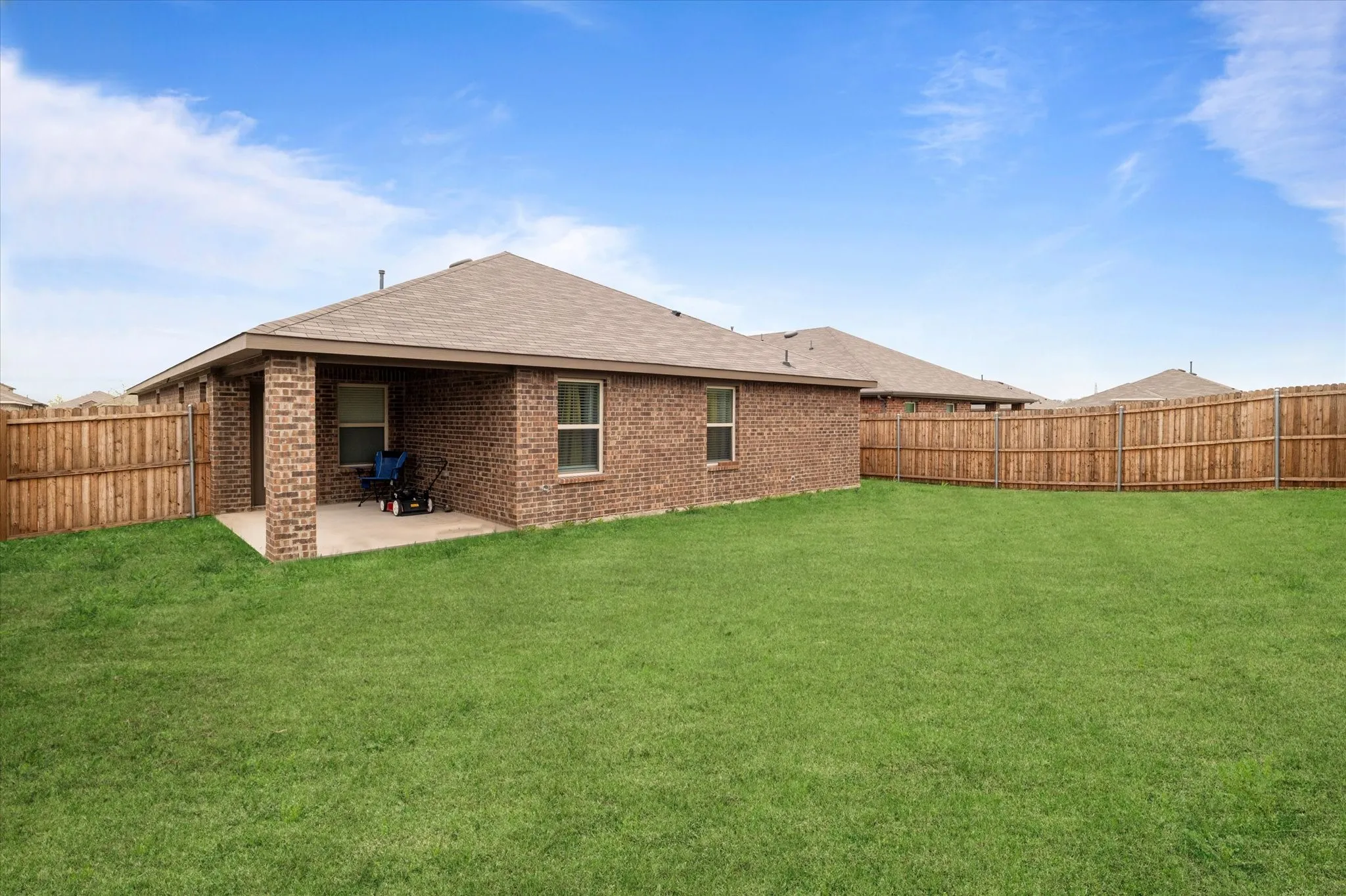 Back of house featuring a shingled roof, a fenced backyard, brick siding, and a patio