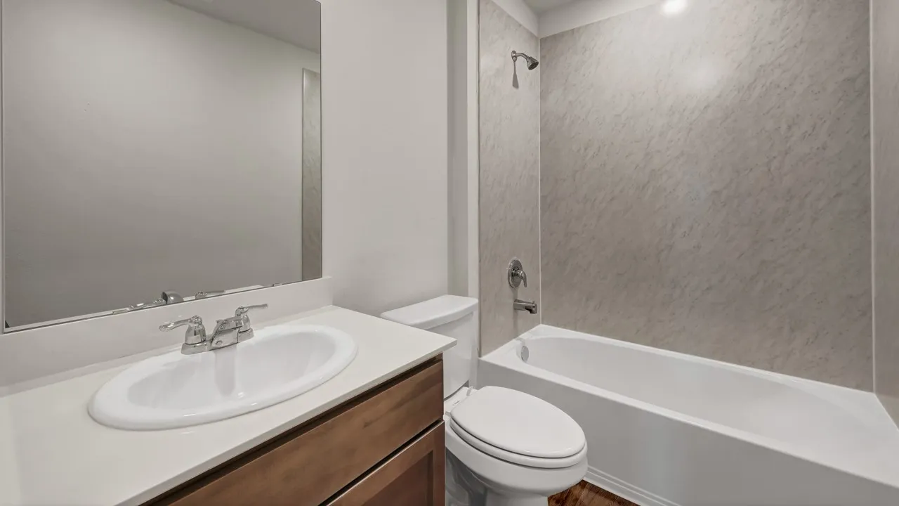 Bathroom featuring a vanity with a white countertop, an undermount sink, a chrome faucet, a rectangular mirror, and a white bathtub with a shower and textured wall surround