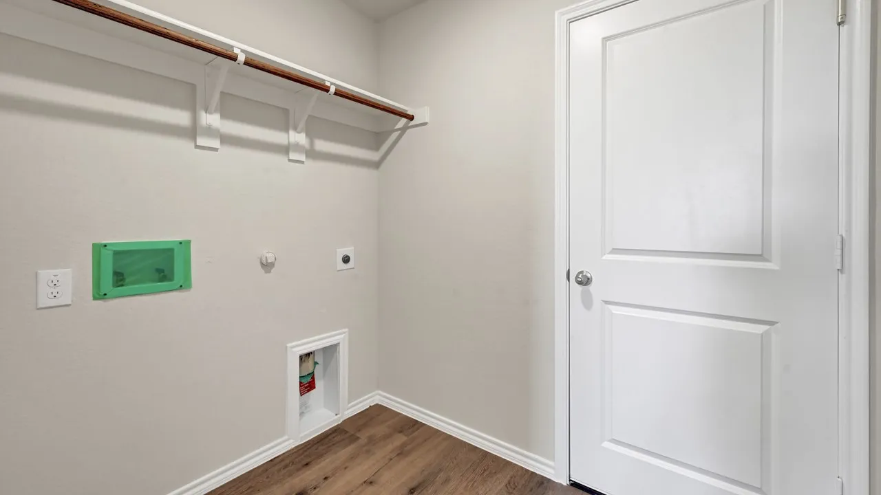 Laundry area with wood-finish flooring, white paneled door, and built-in shelving with hanging rod