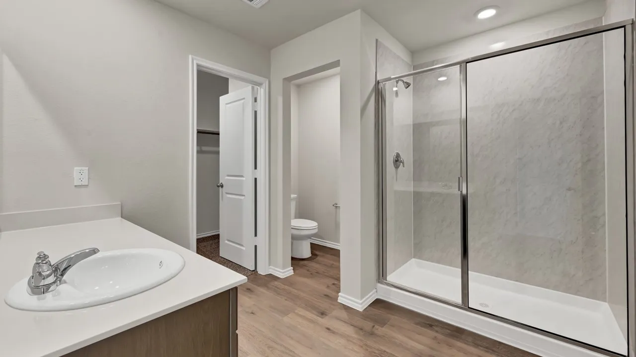 Vanity with undermount sink and chrome faucet, wood-finish flooring, and a glass-enclosed shower with textured wall panels