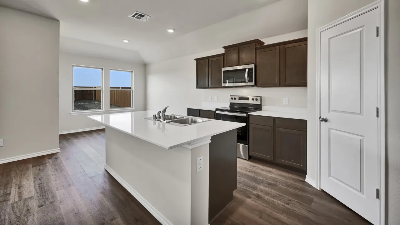 Contemporary kitchen featuring a center island with an undermount sink, white countertops, dark wood-finish cabinetry, and stainless steel appliances