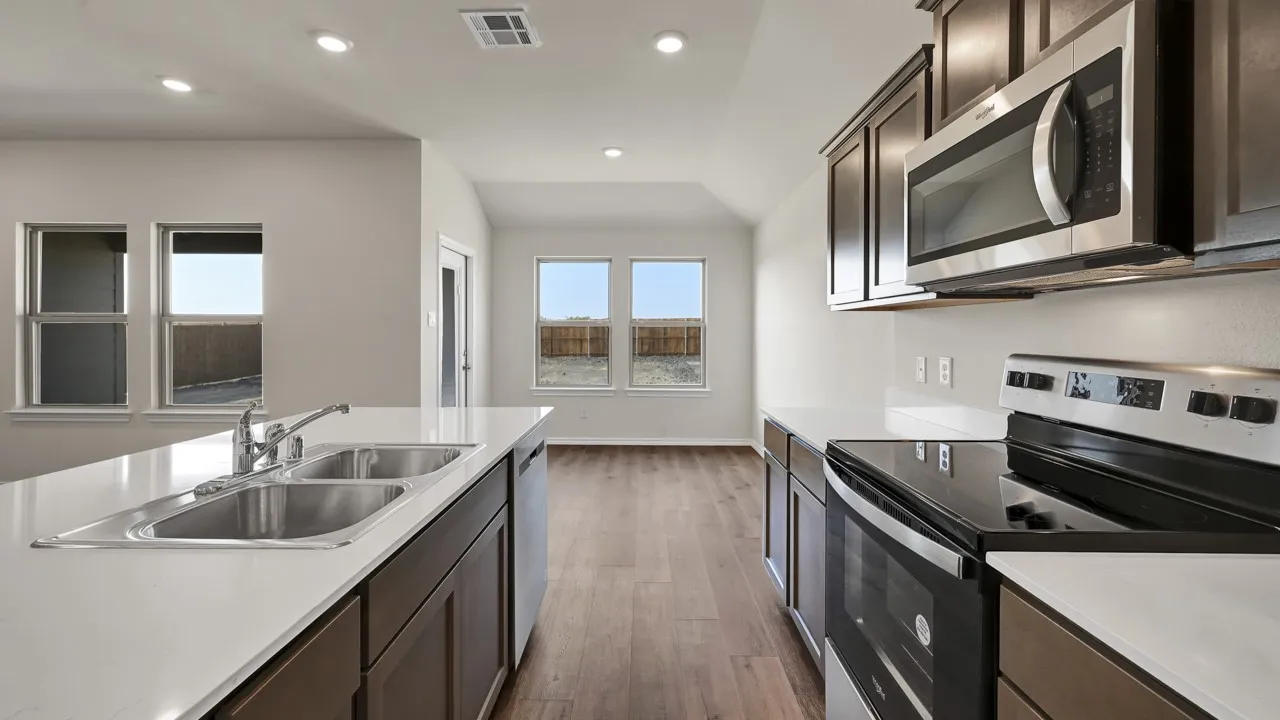 Kitchen featuring a double basin sink, stainless steel appliances, dark wood-finish cabinetry, light-colored countertops, and wood-finish flooring