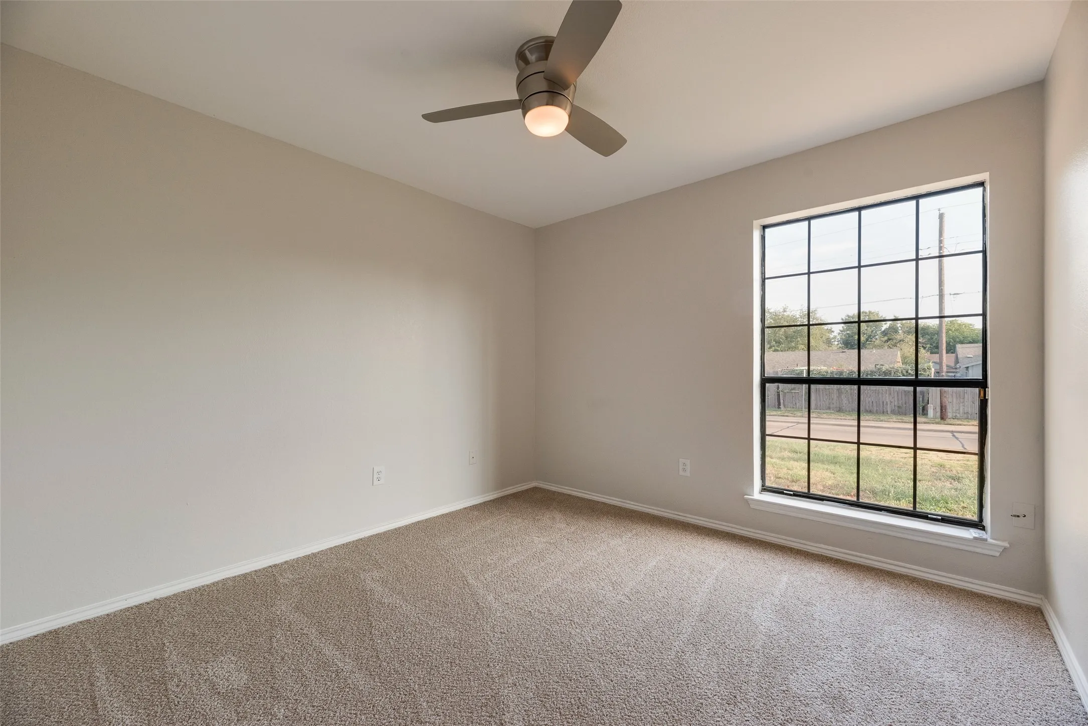 Carpeted flooring, neutral wall tones, ceiling fan with integrated lighting, and a large multi-pane window