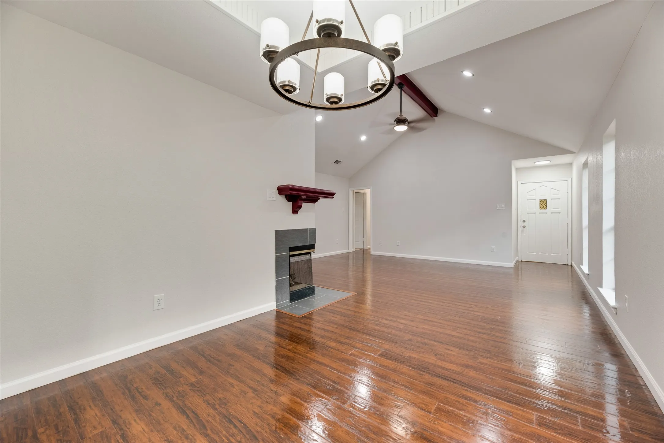 Vaulted ceiling with exposed beam, wood-finish flooring, recessed lighting, and a fireplace with a dark tile surround and wood mantel