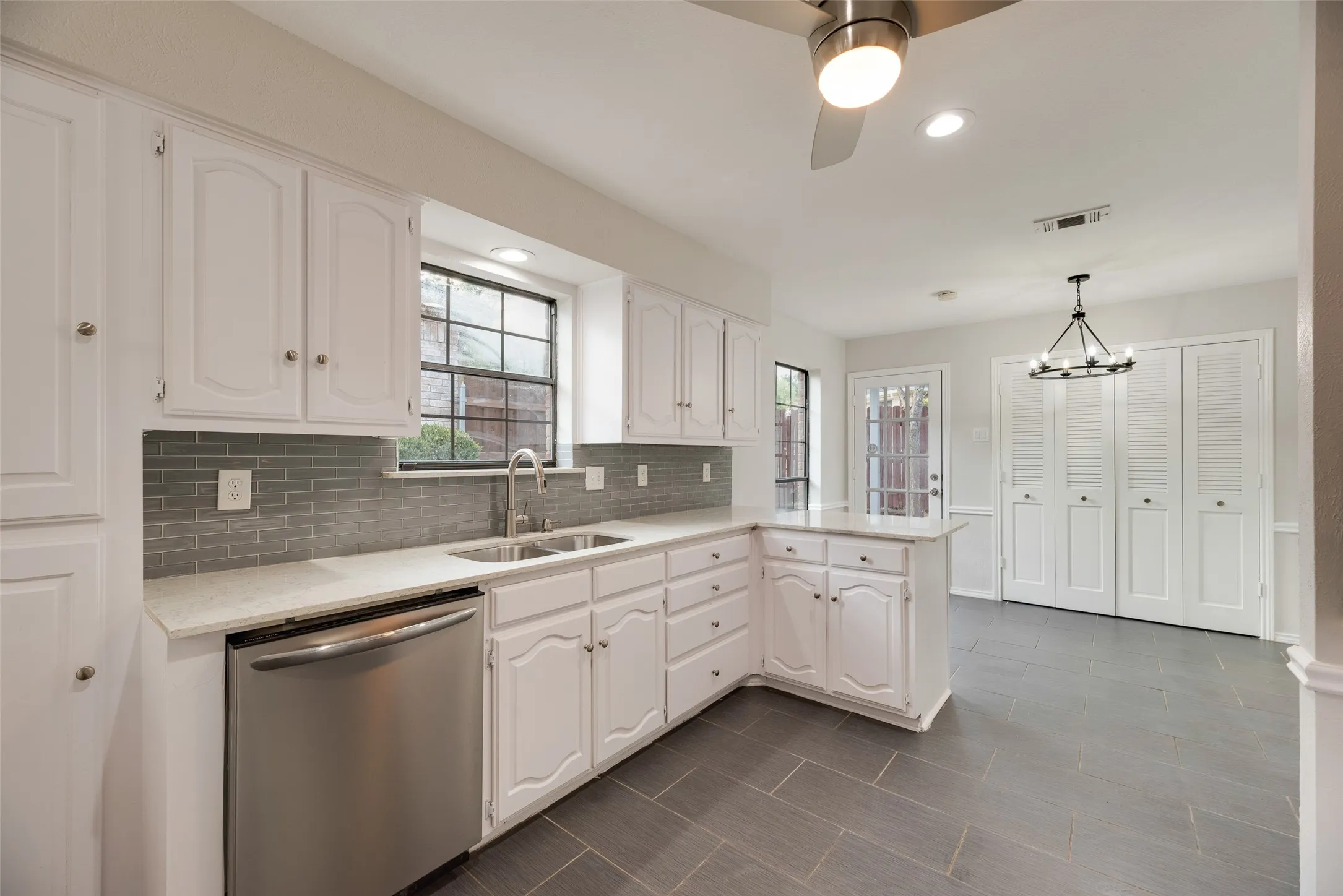 Kitchen featuring white cabinetry, light-toned countertops, a tile backsplash, stainless steel dishwasher, and tiled flooring