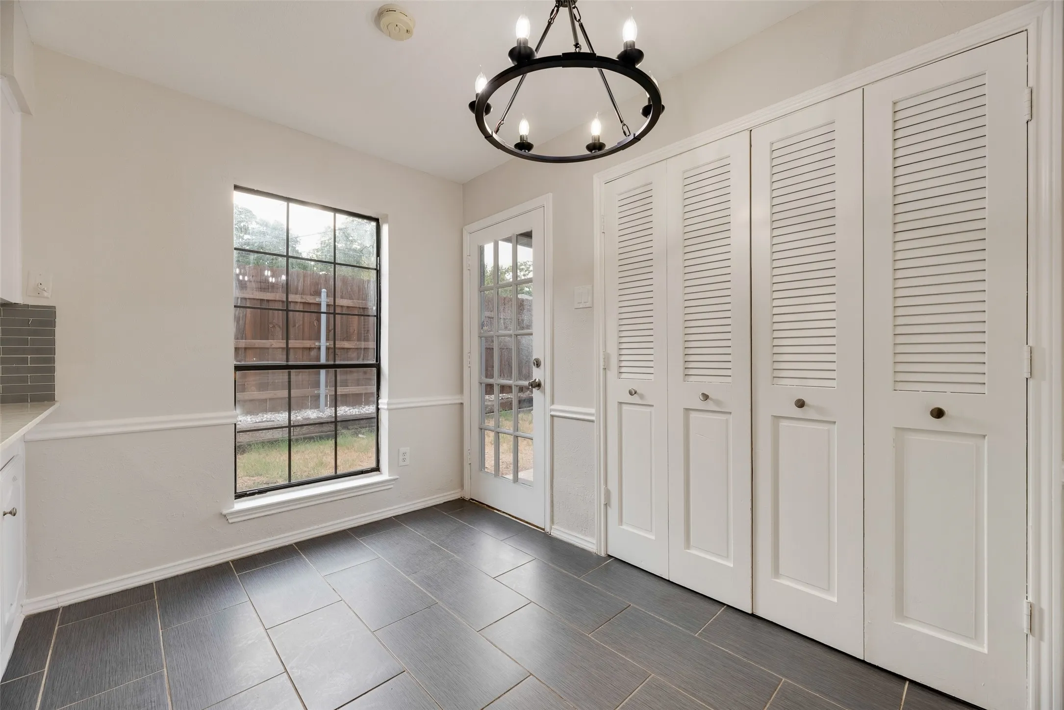 Dark tile flooring, white wainscoting, white louvered bifold doors, a glass-panel exterior door, and a black metal chandelier