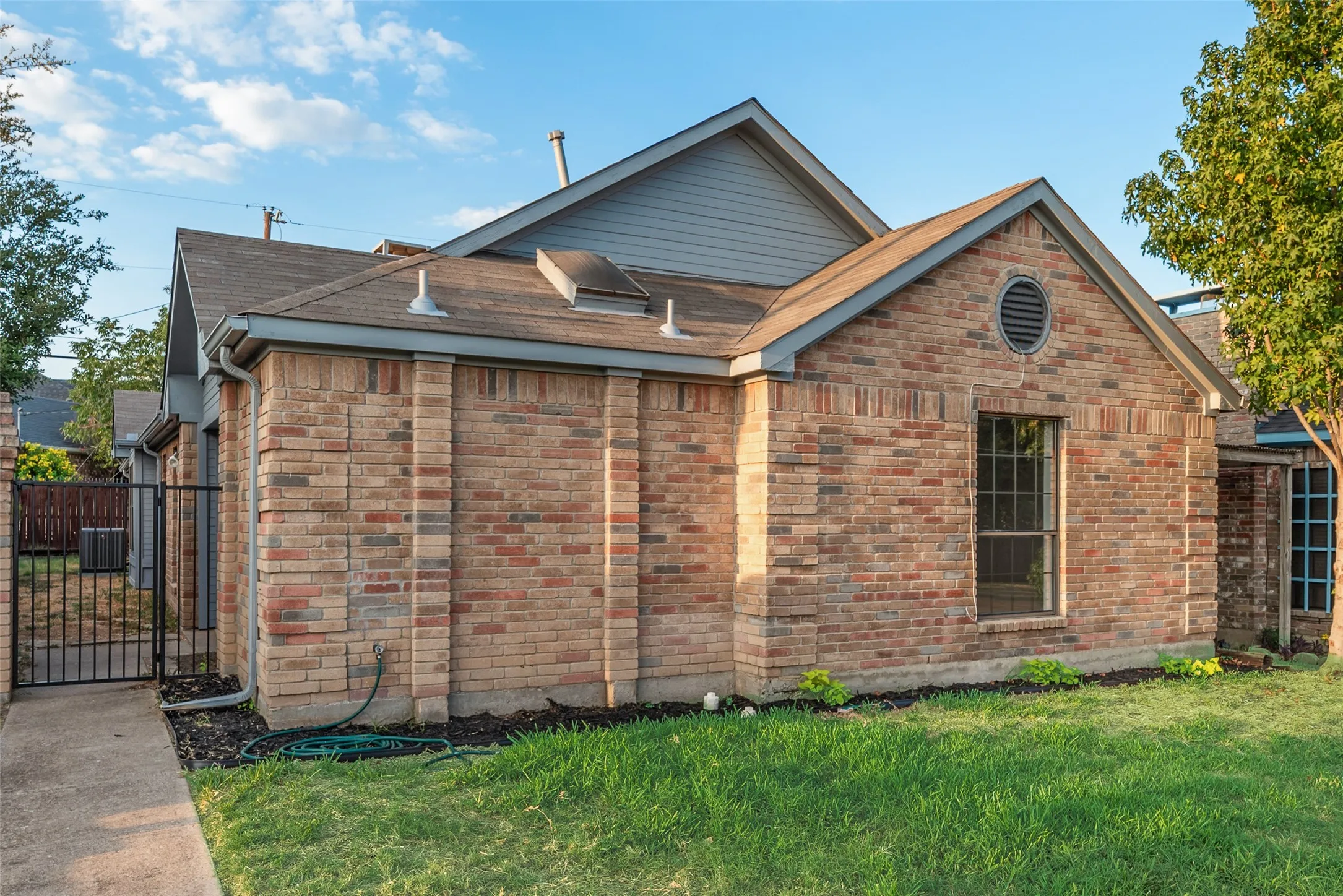 Brick exterior with an ornamental circular vent, a prominent window, a metal gate, and partial yard space